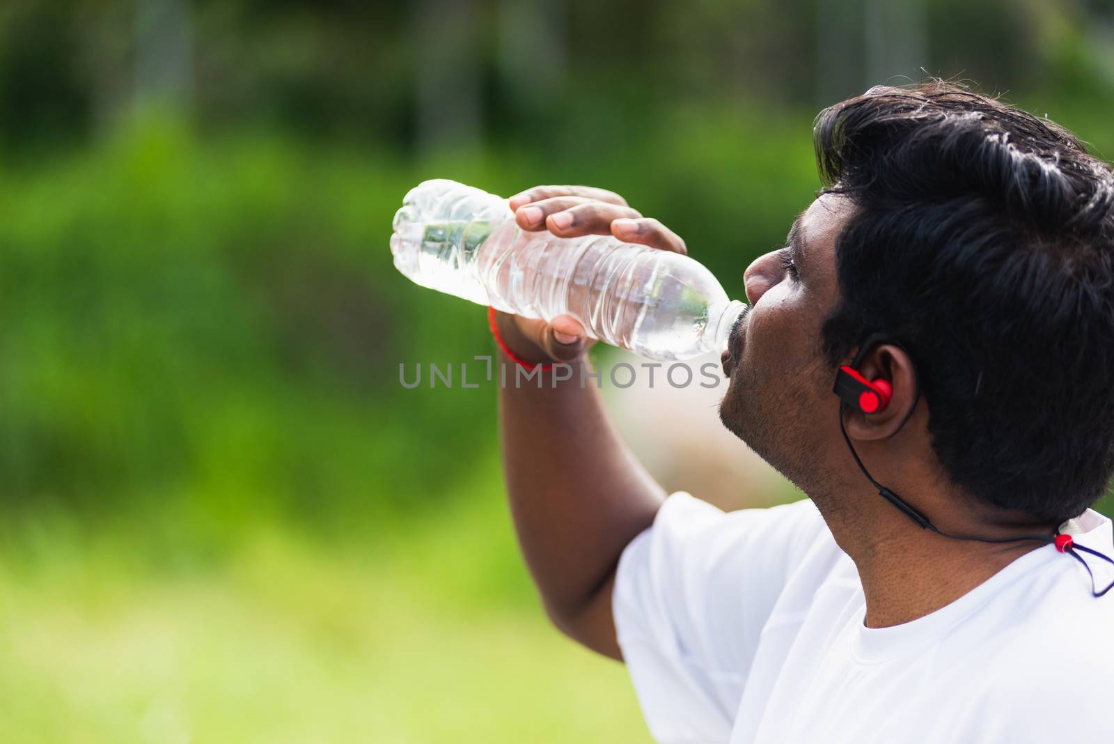 Close up Asian young sport runner black man wear athlete headphones he drinking water from a bottle after running at the outdoor street health park, healthy exercise workout concept