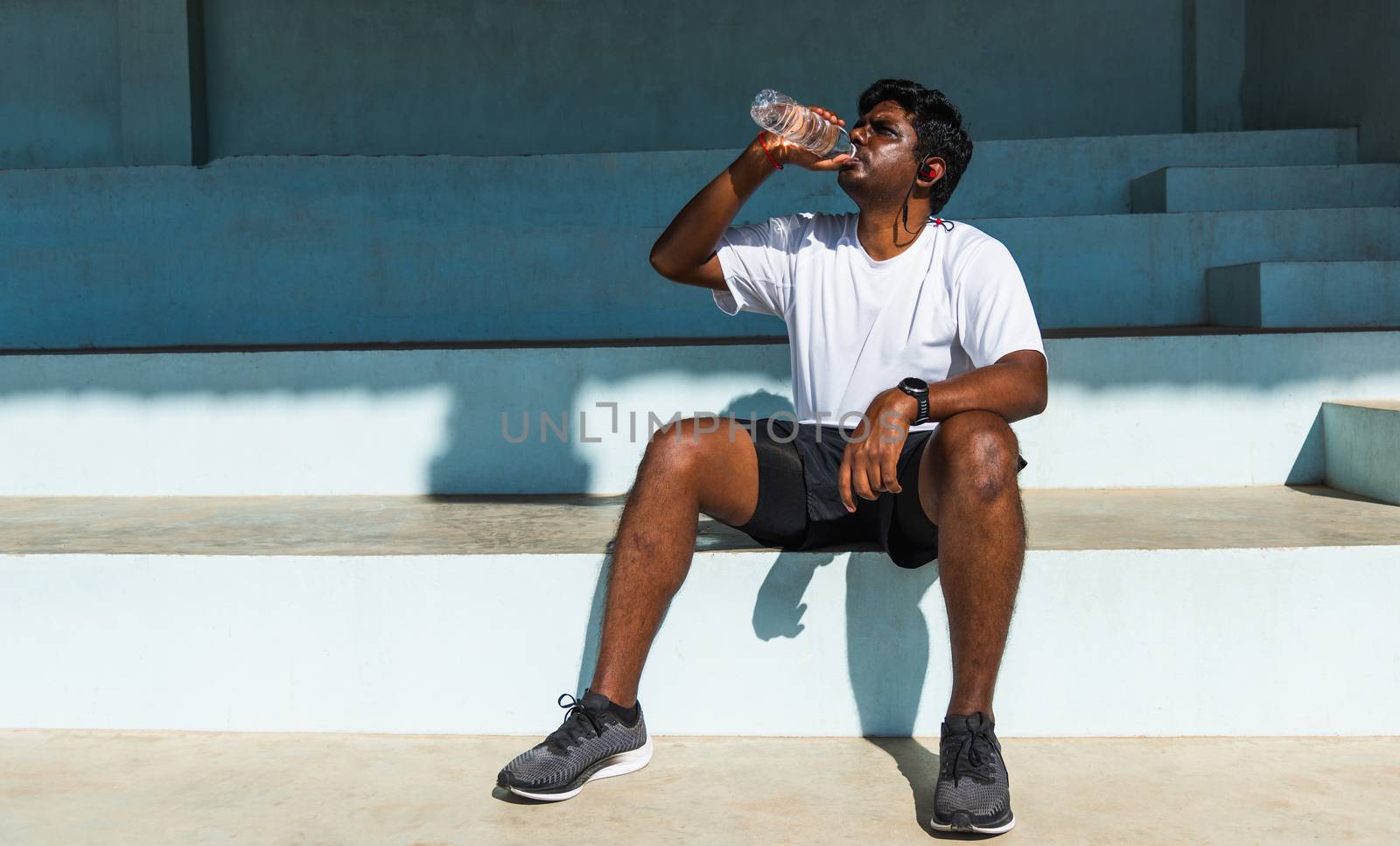 Close up Asian young sport runner black man wear athlete headphones he drinking water from a bottle after running at the outdoor street health park, healthy exercise workout concept