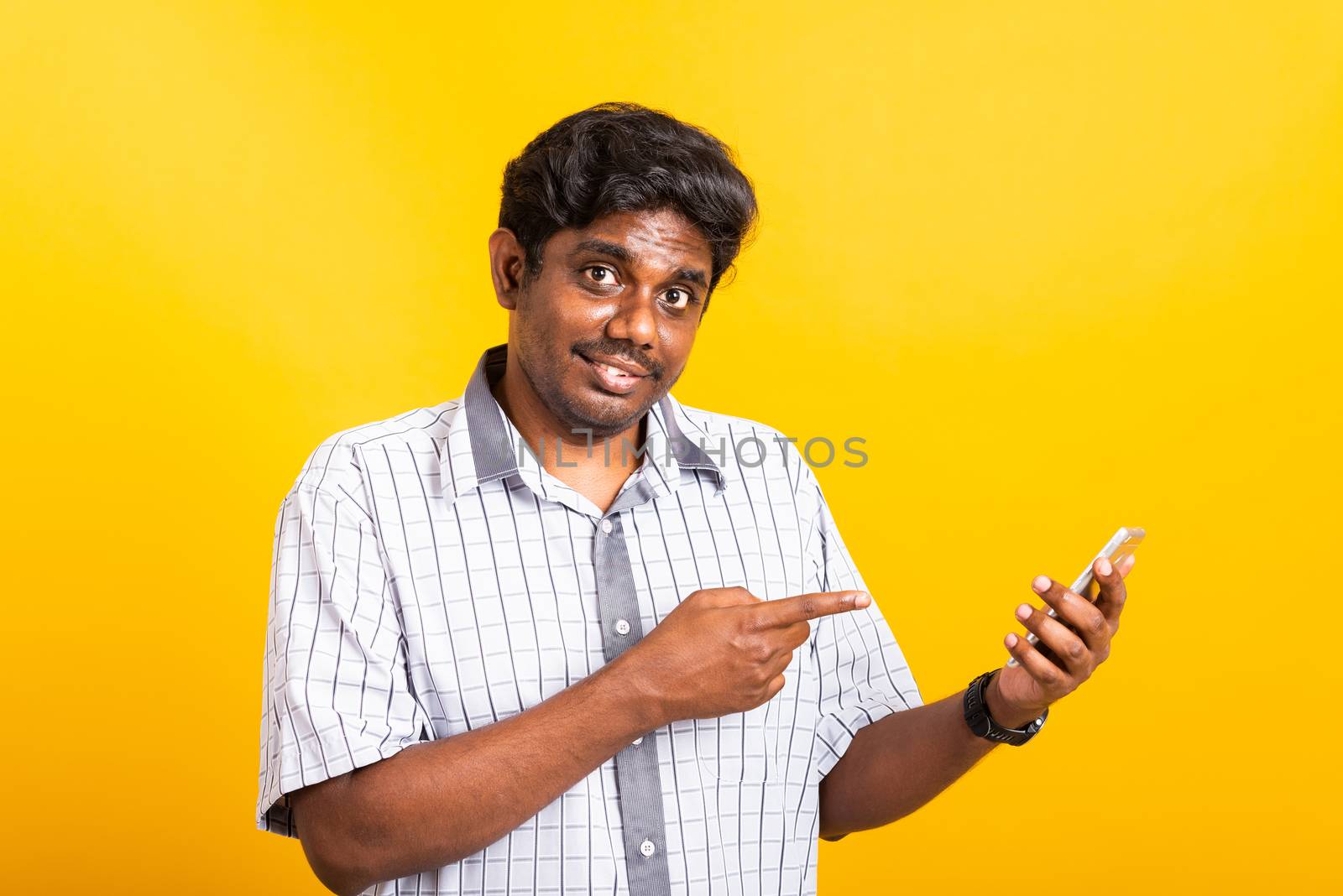 Asian happy portrait young black man smile standing wear shirt making finger pointing on smart digital mobile phone blank screen isolated, studio shot yellow background with copy space