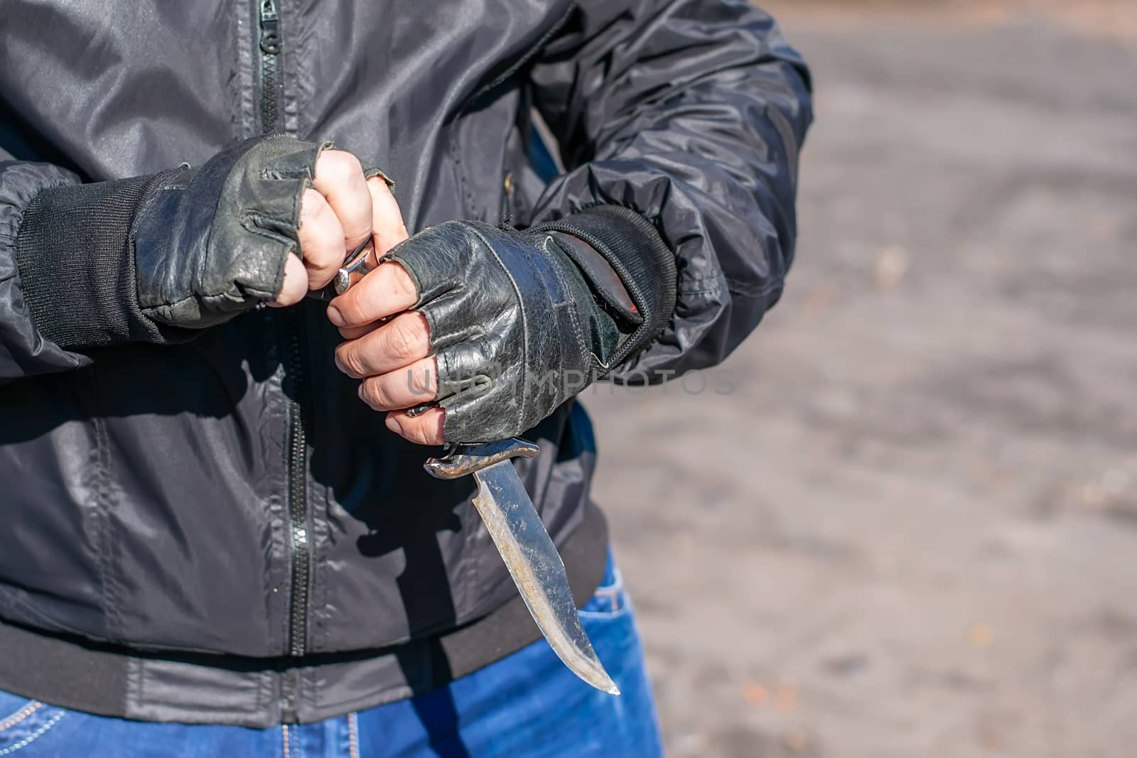 knife in the hands of a bandit in a black jacket and leather gloves by jk3030