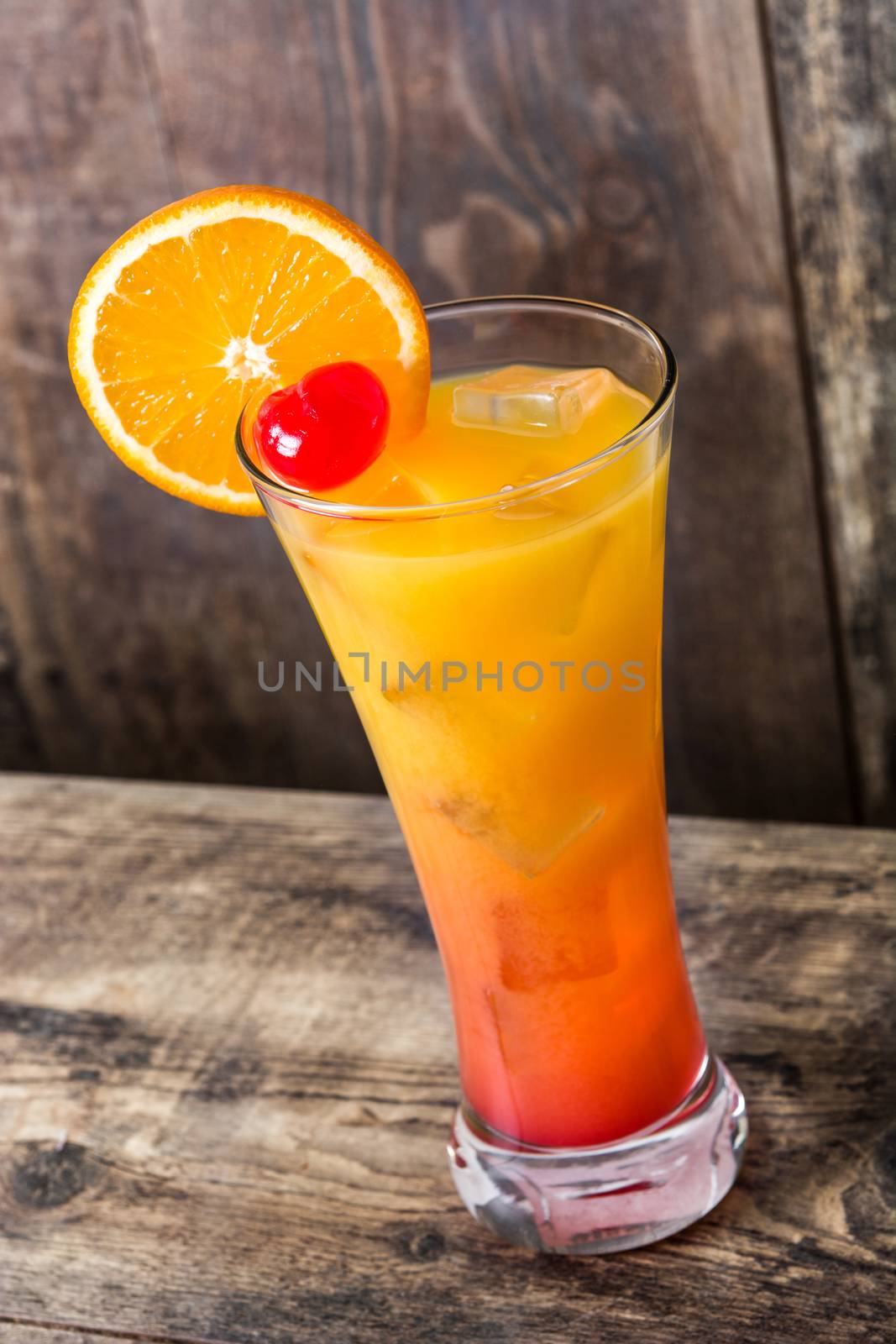 Tequila sunrise cocktail in glass on wooden table. by chandlervid85