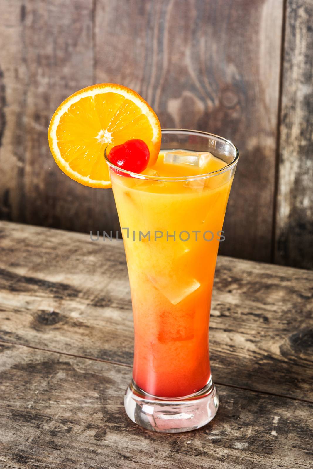 Tequila sunrise cocktail in glass on wooden table.