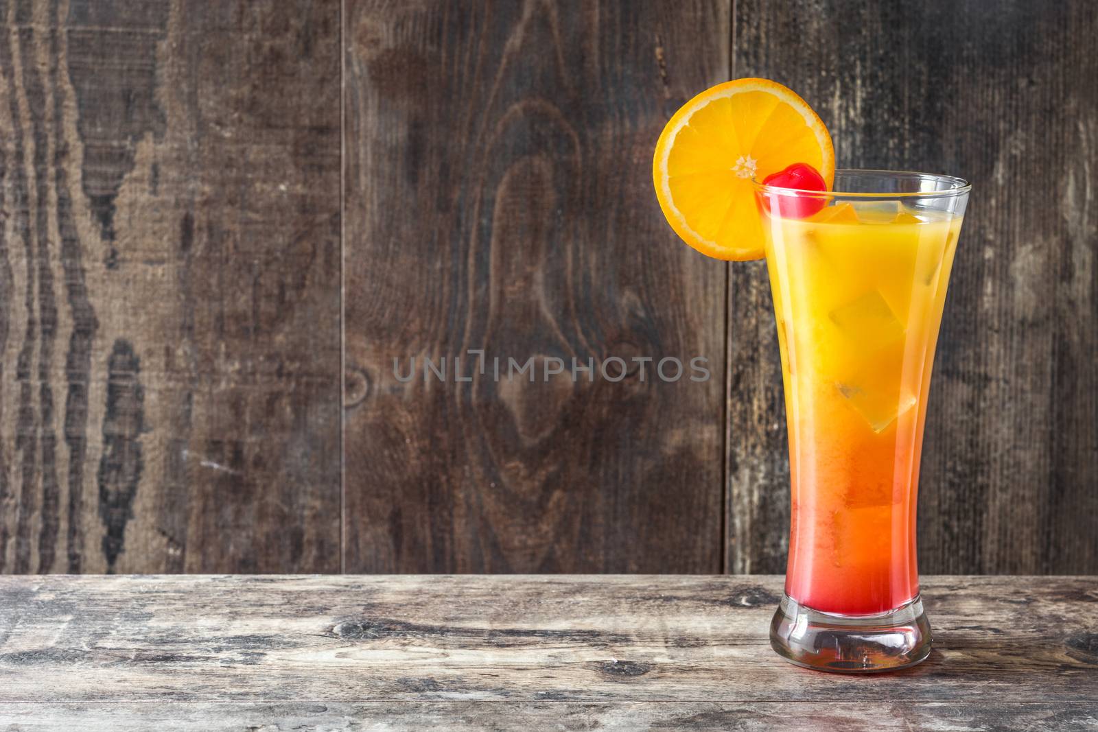 Tequila sunrise cocktail in glass on wooden table.