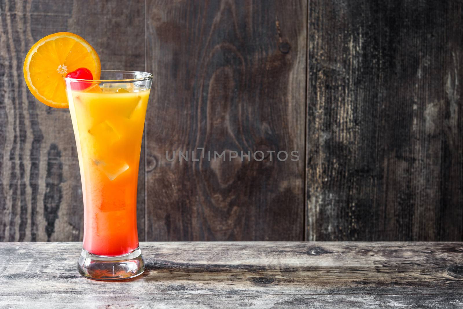 Tequila sunrise cocktail in glass on wooden table. by chandlervid85