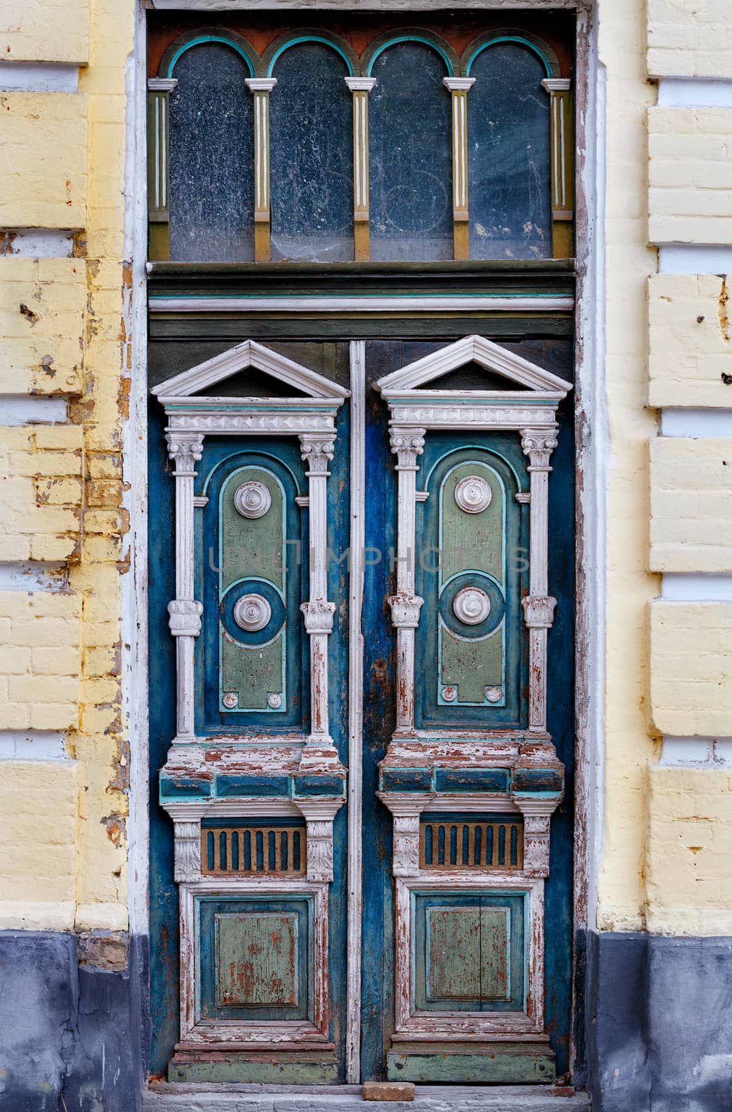 Old weathered wooden entrance doors with carved elements and a symmetrical pattern on the facade of an old house. by Sergii