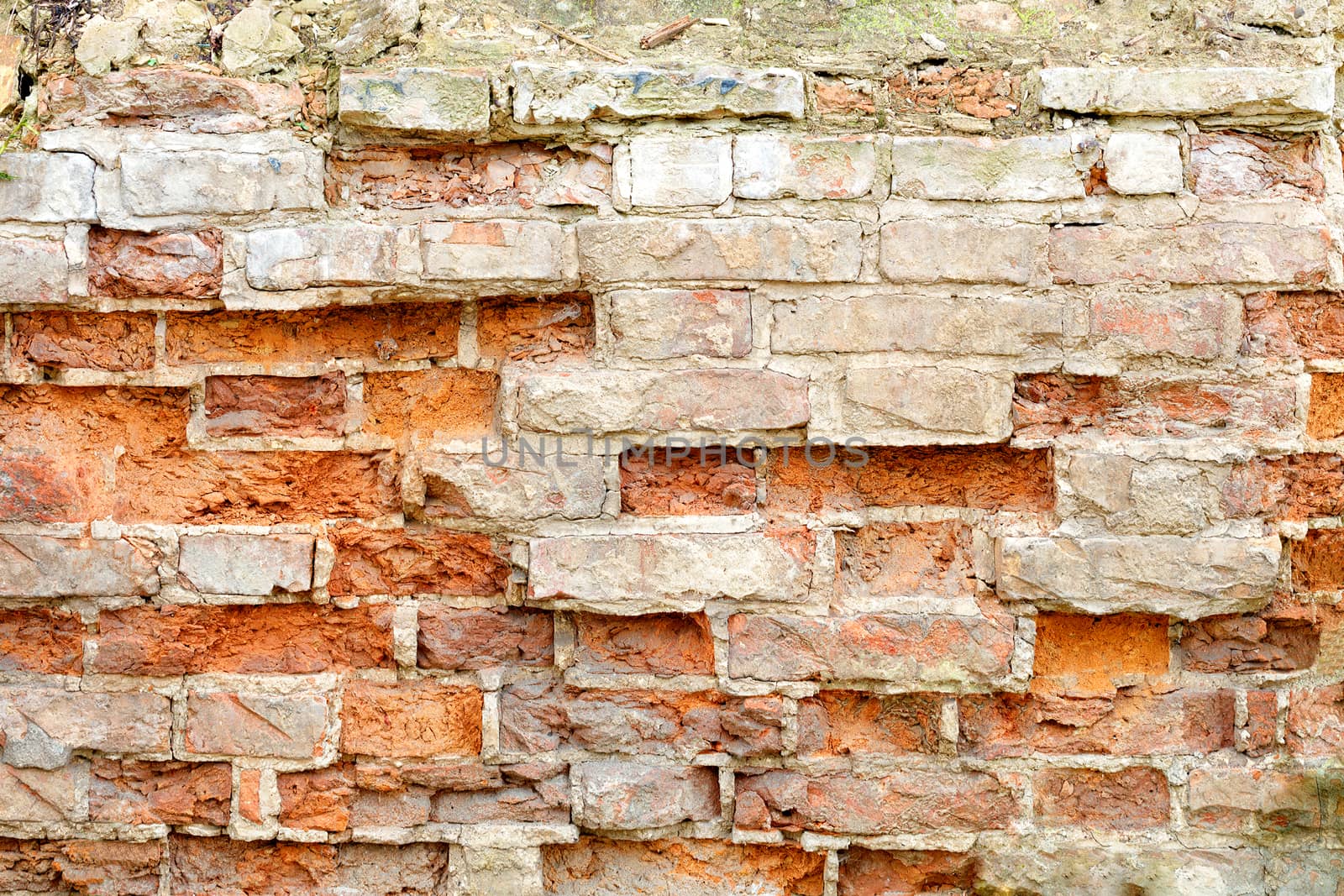 Old ruined red brick wall with cracked and broken bricks. Background texture of debris and piece of brickwork.