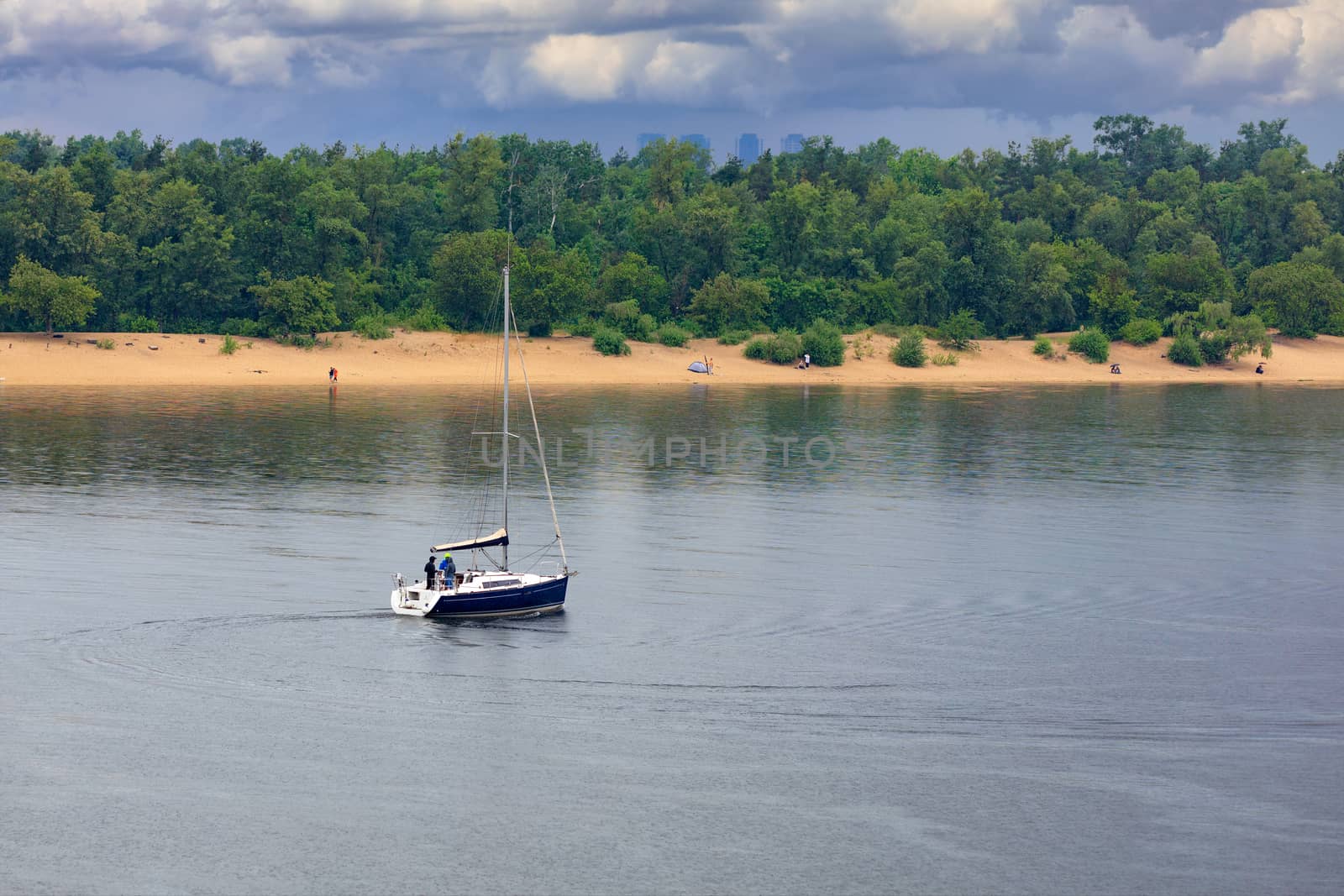Sailing boat drifts in the middle of the river in the rain against the background of the riverbank and green spaces. by Sergii