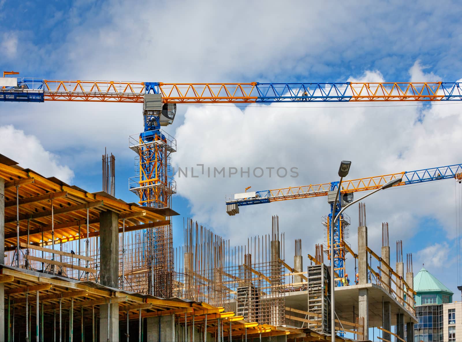Tower cranes work at the construction site of a multi-storey residential building against a blue sky and white clouds, copy space.