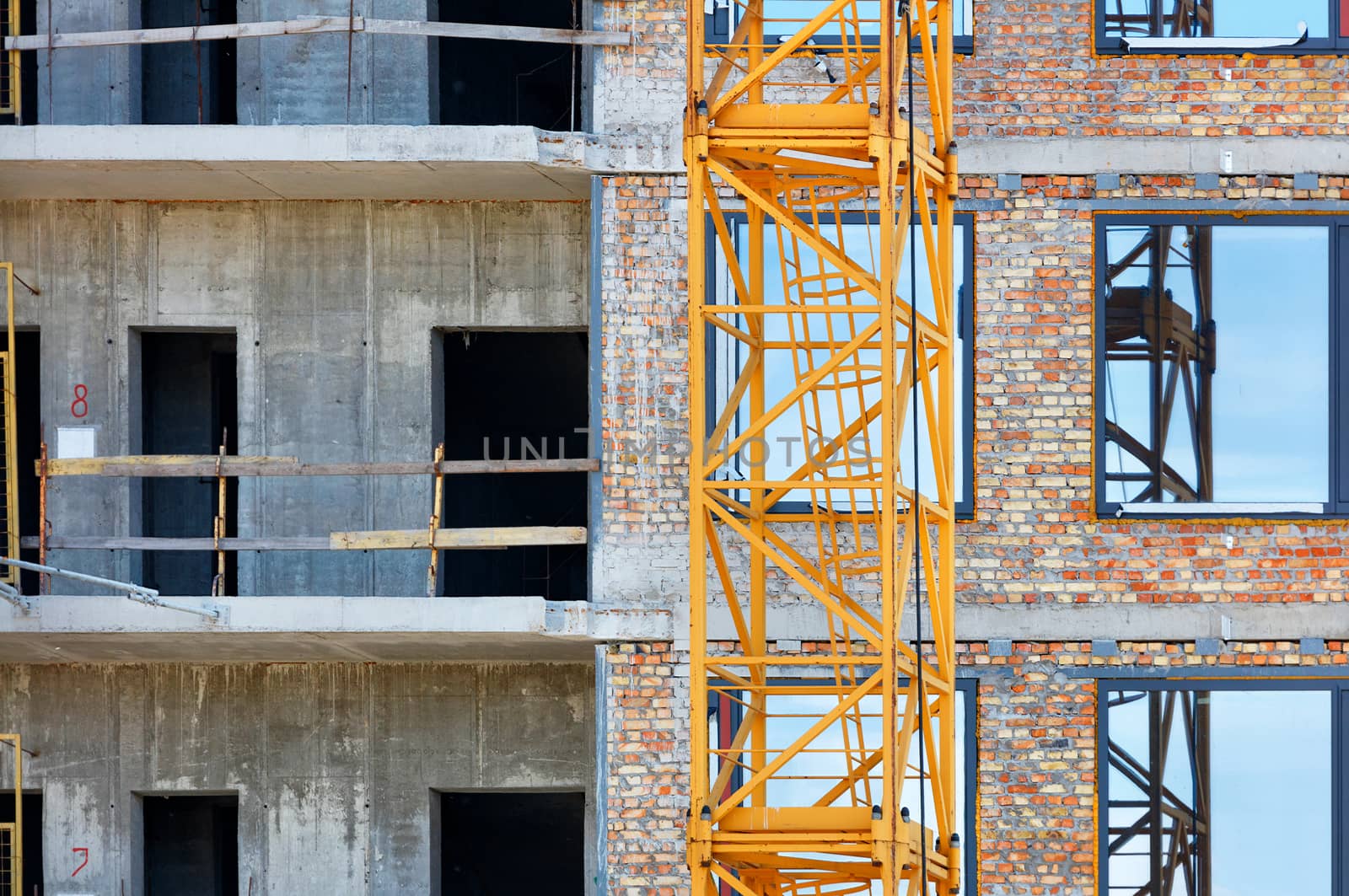 A fragment of the facade of a reconstructed house under construction, a tower crane and a blue sky are reflected in the glass windows of the building.