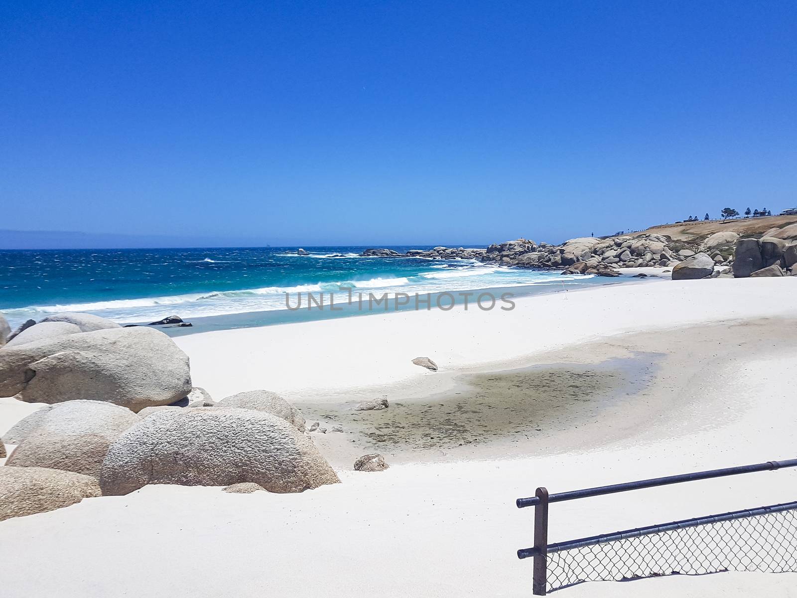 Camps Bay Beach behind fence and rocks in Cape Town.