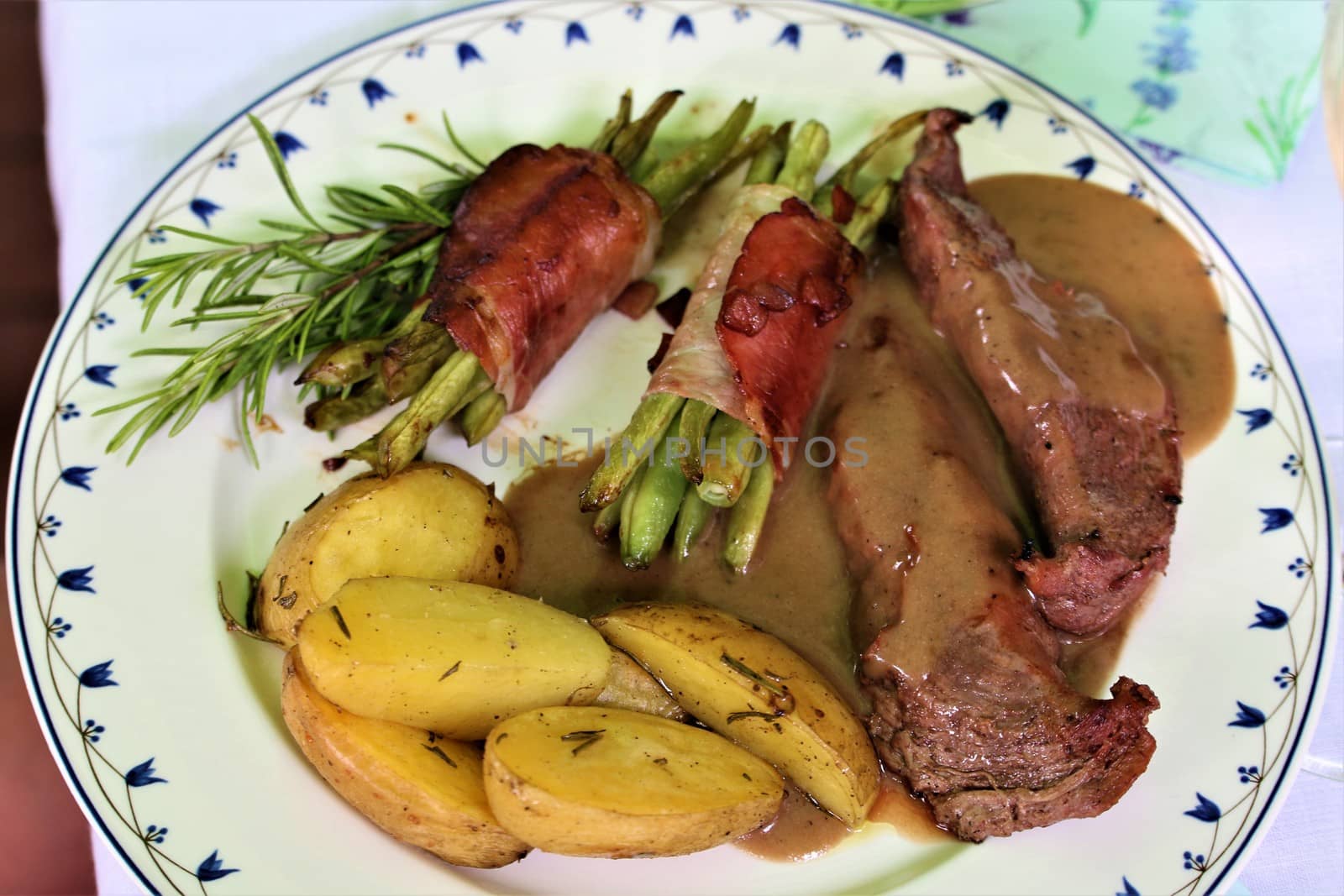 grilled lamb fillet with beans wrapped in bacon and potato wedges on a plate