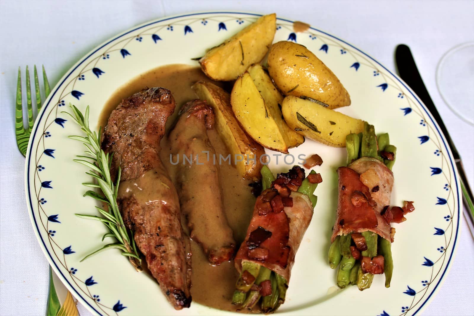 grilled lamb fillet with beans wrapped in bacon and potato wedges on a plate