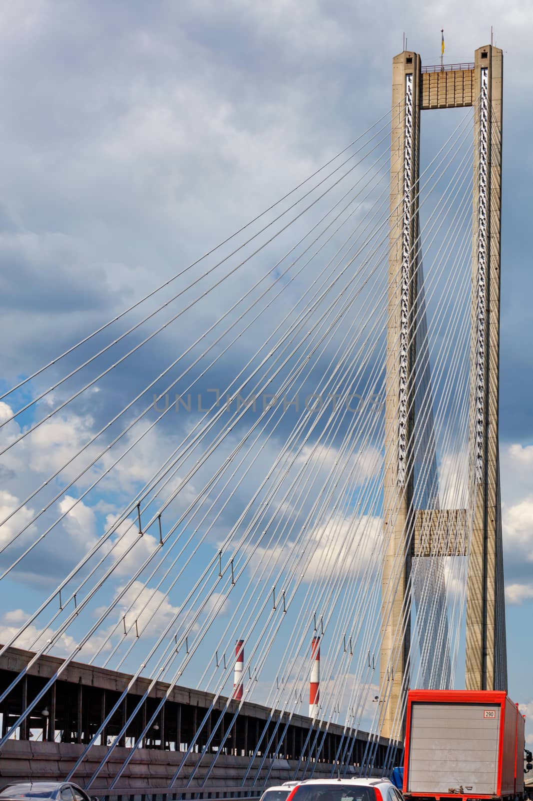 The arrow of the cable-stayed South Bridge in Kyiv, Ukraine, with the flag of Ukraine on top against the background of the cloudy sky. by Sergii