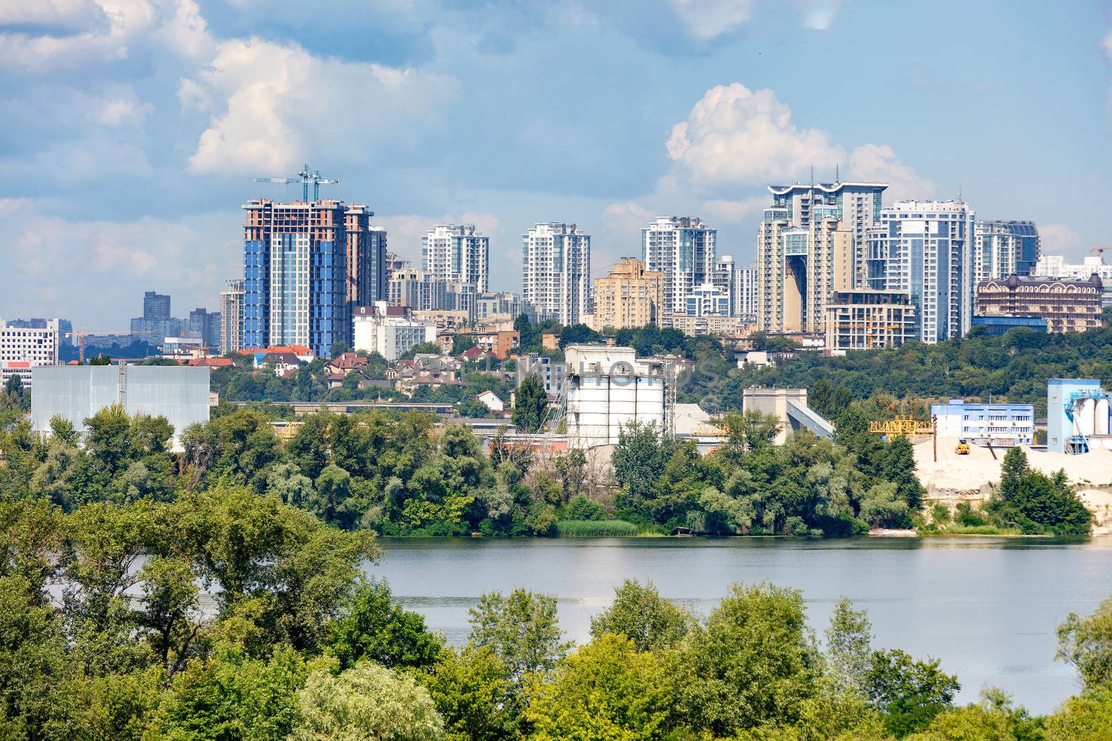 Construction of new high-rise buildings on the right bank of the Dnipro River in Kyiv, a view of the facades of multi-storey residential buildings among private houses and a blue cloudy sky, copy space.