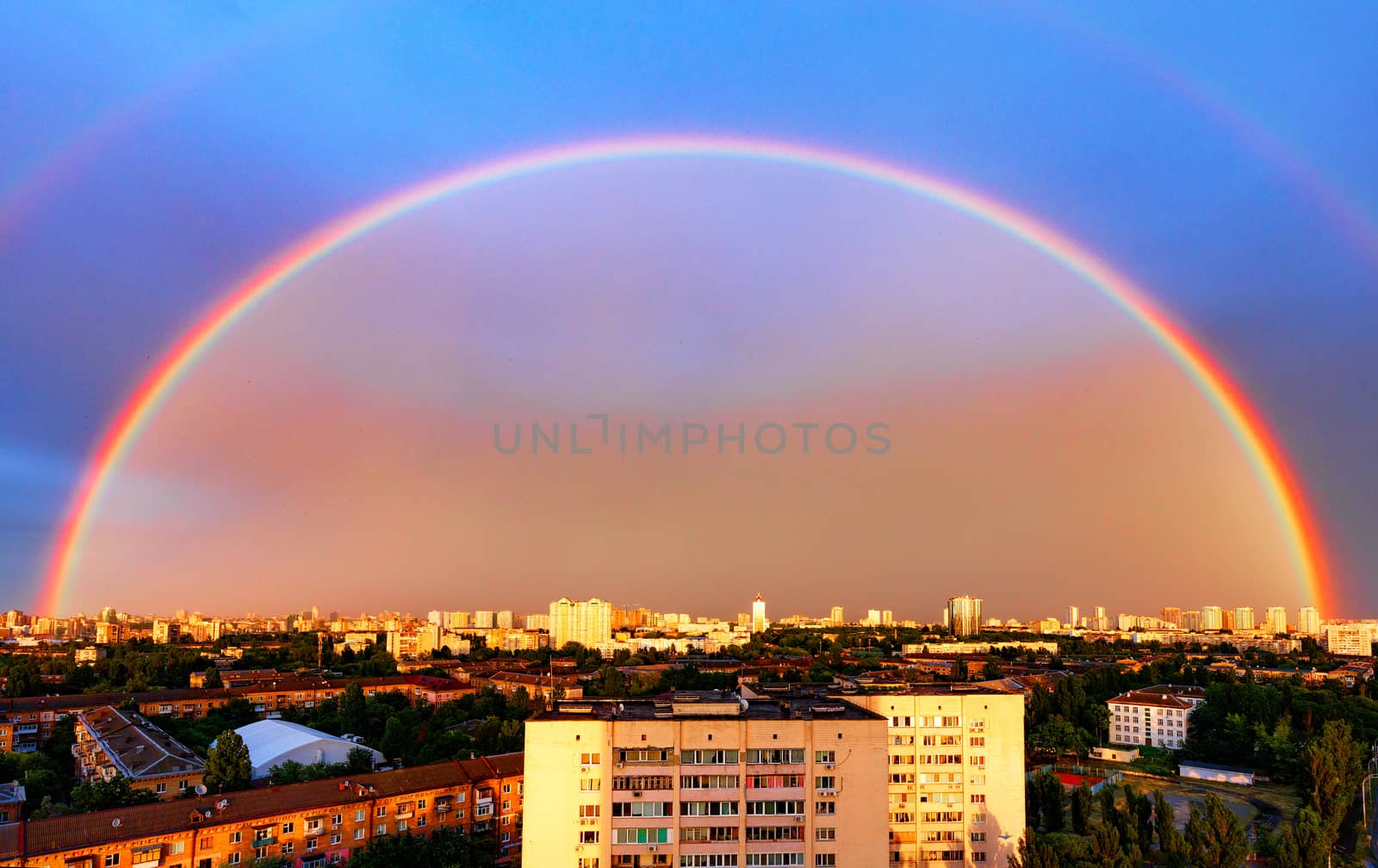 Panorama of an urban residential area and a huge rainbow illuminated by the sun against the backdrop of the evening sky.