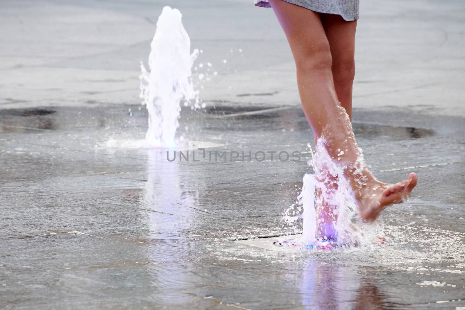 a girl touches a fountain on the sidewalk with her bare foot.