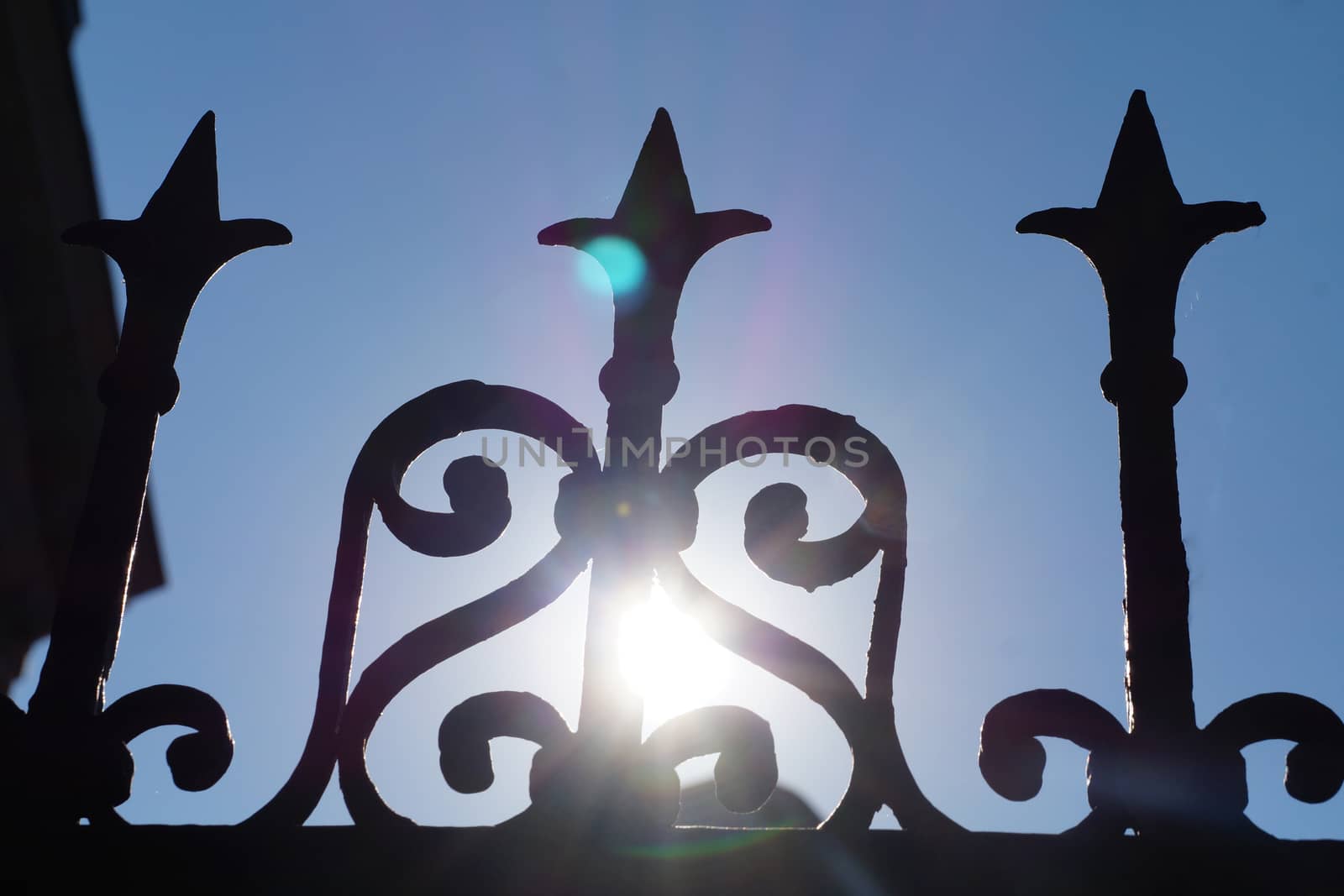 fragment of a forged fence against the background of the sun and clear sky, bottom view