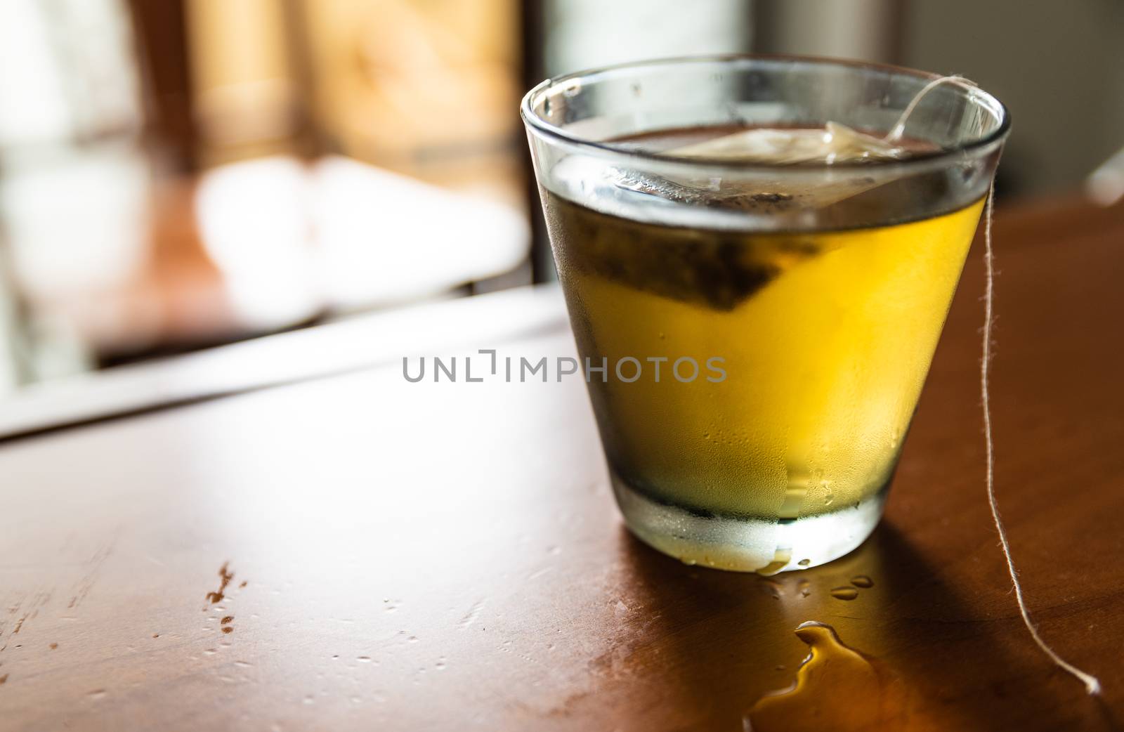 Close-up image of a cold herbal tea: the glass is covered with condensation. The sachet is infused in the glass.