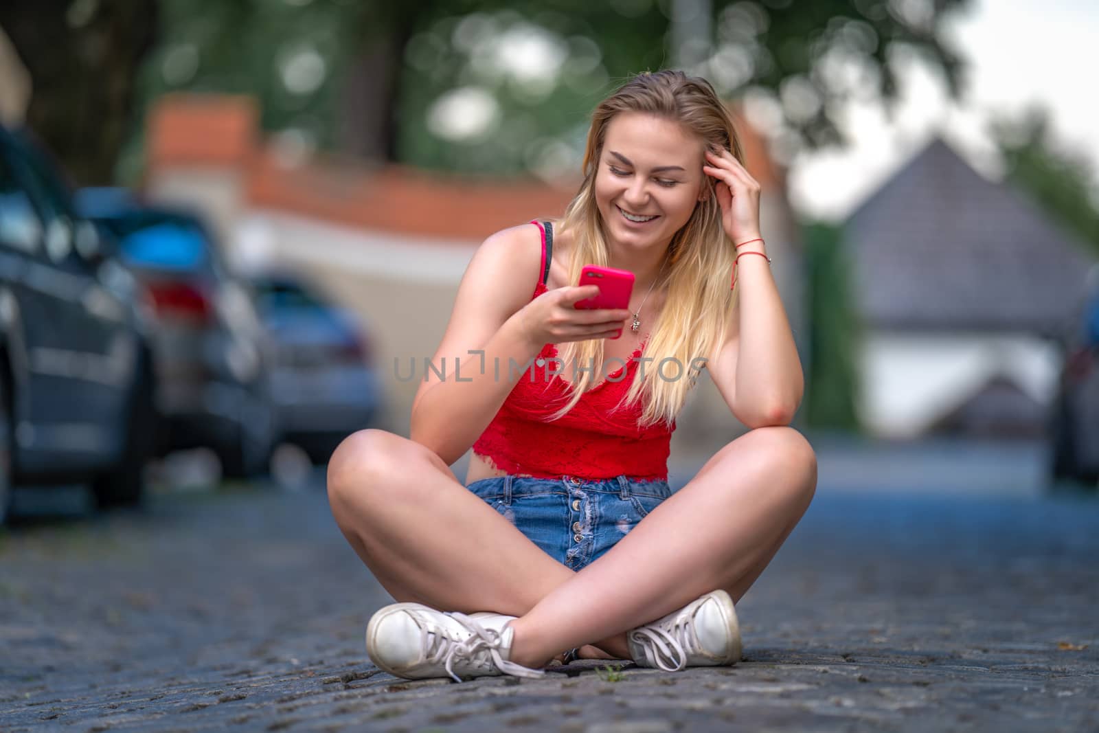 portrait of a beautiful young woman sitting on the pavement in the city streets using a smartphone.