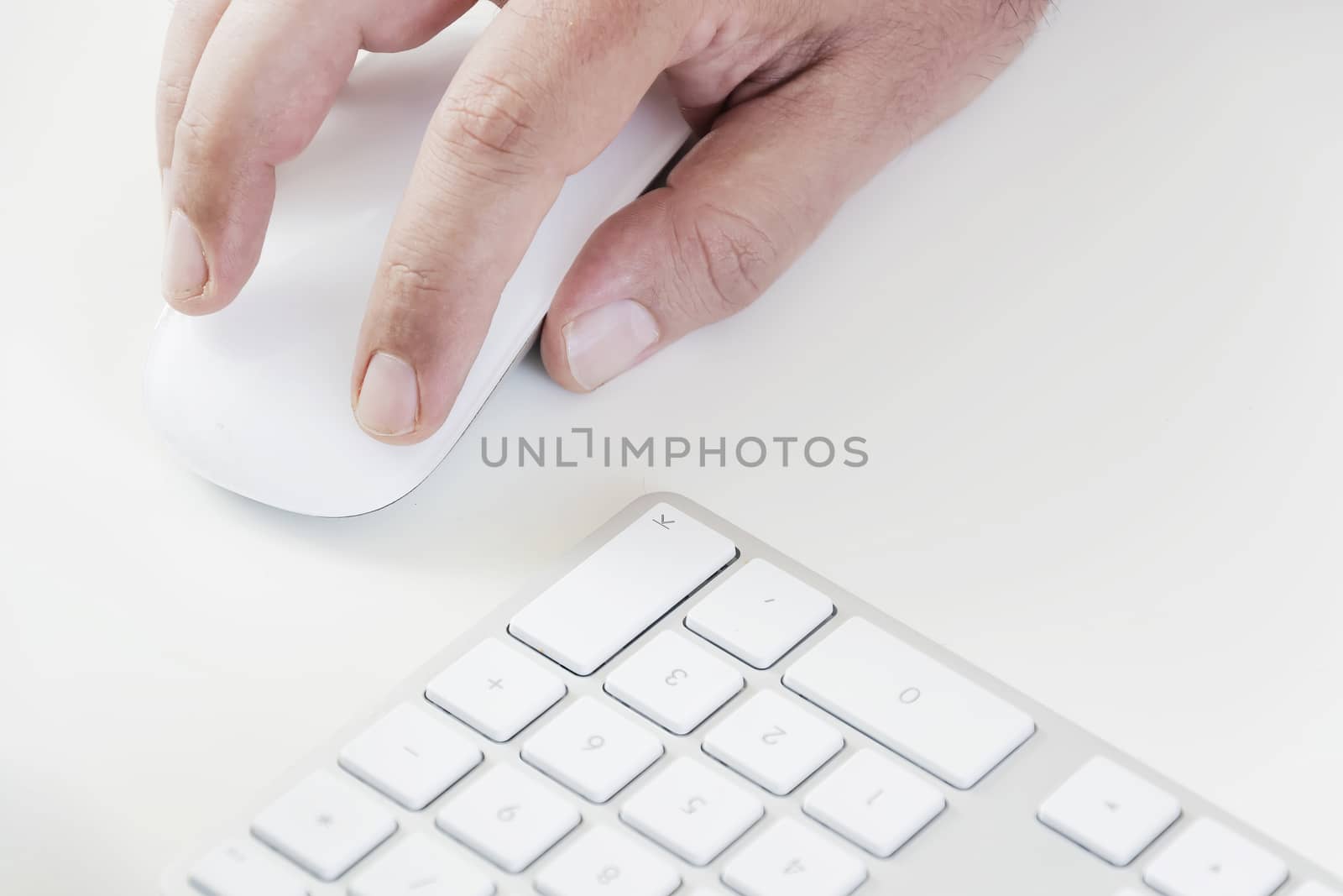 male hand clicking on a white mouse with a white keyboard on the right. White table in a office by rarrarorro