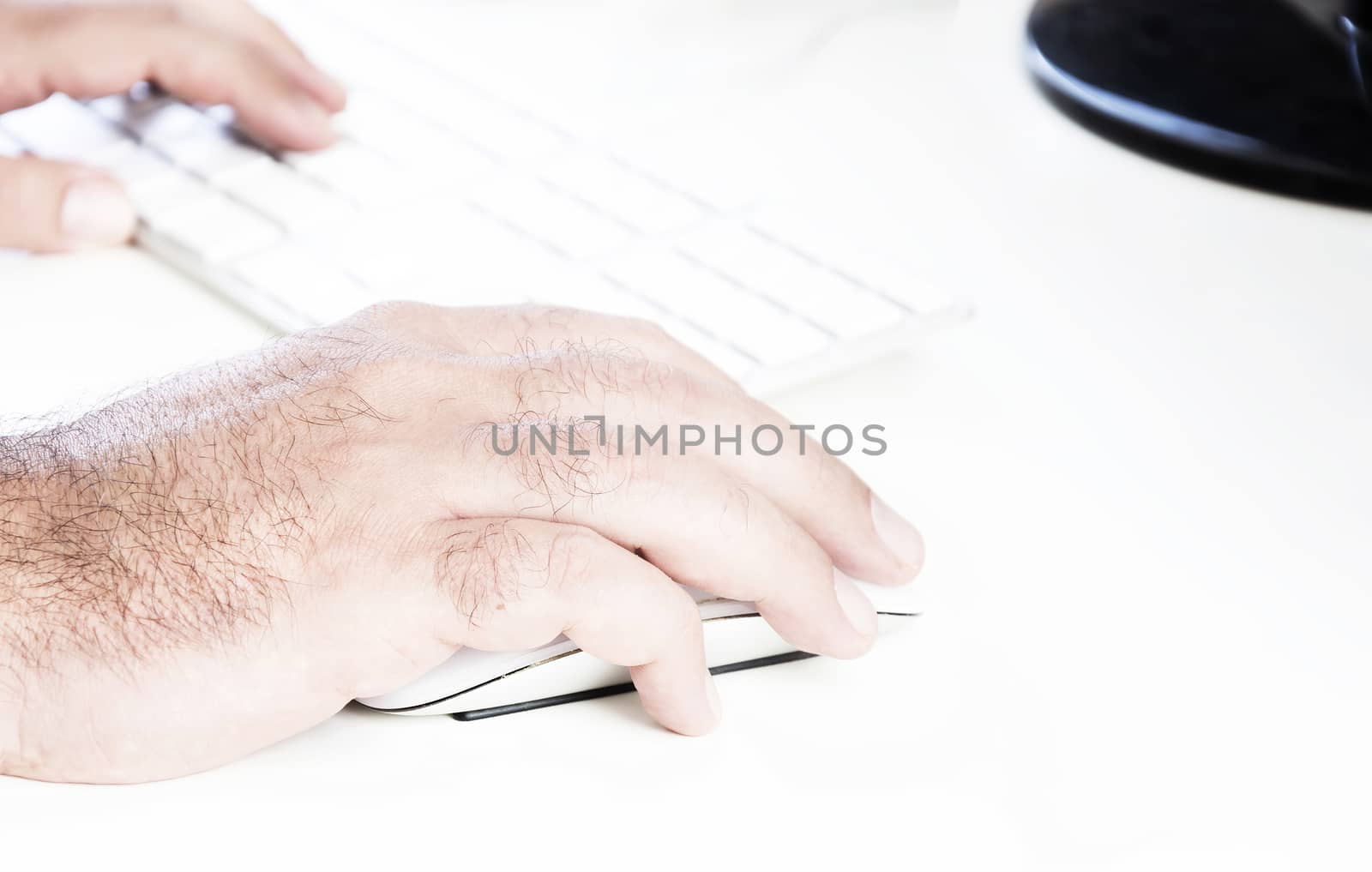 male hand clicking on a white mouse with a white keyboard on the right. White table in a office by rarrarorro