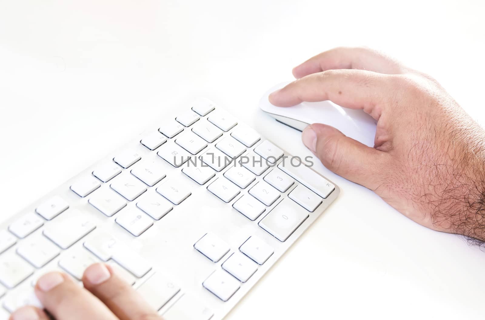 male hand clicking on a mouse and typing on a white keyboard on a white table. White background.