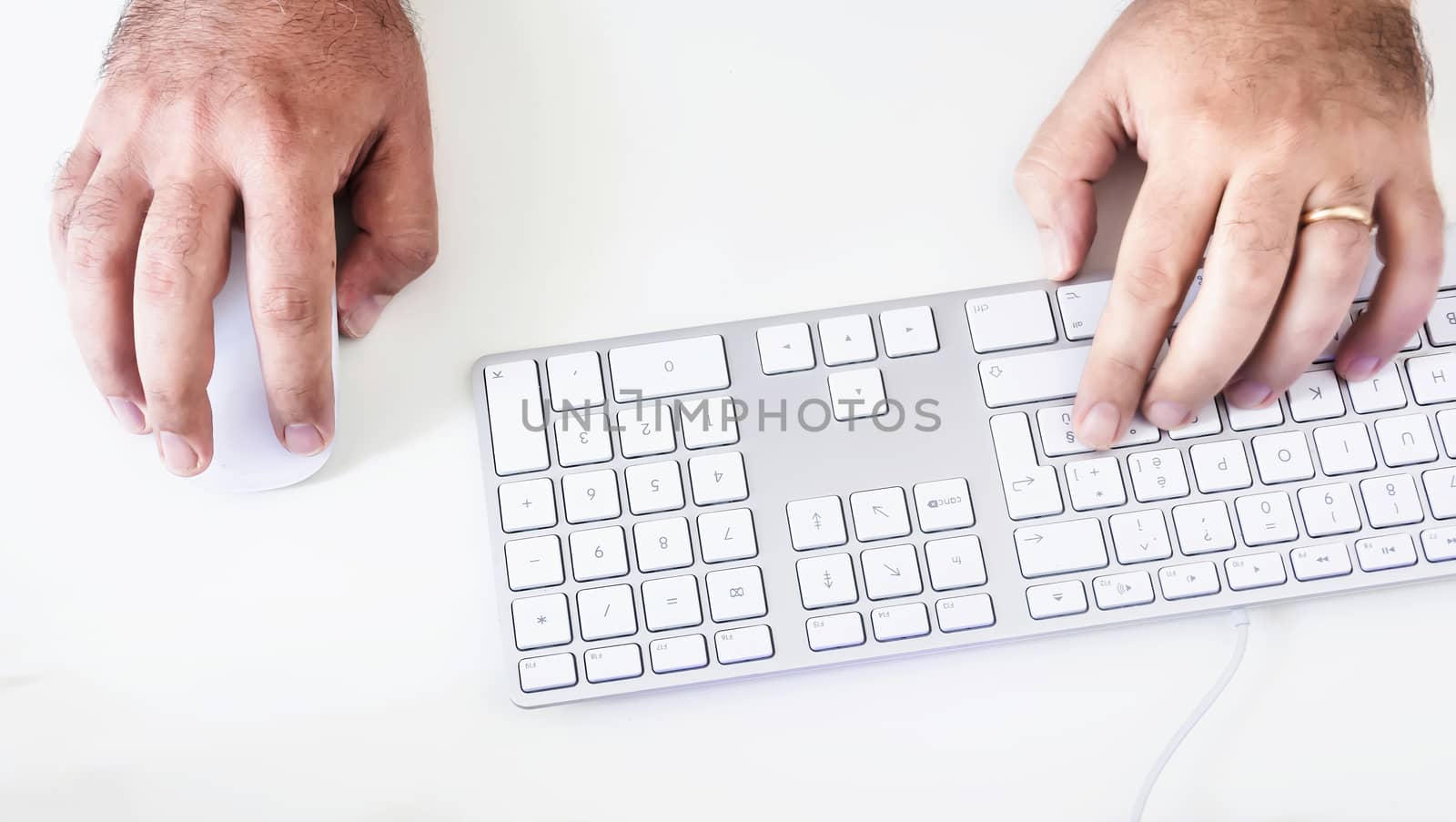 male hand clicking on a mouse and typing on a white keyboard on a white table by rarrarorro