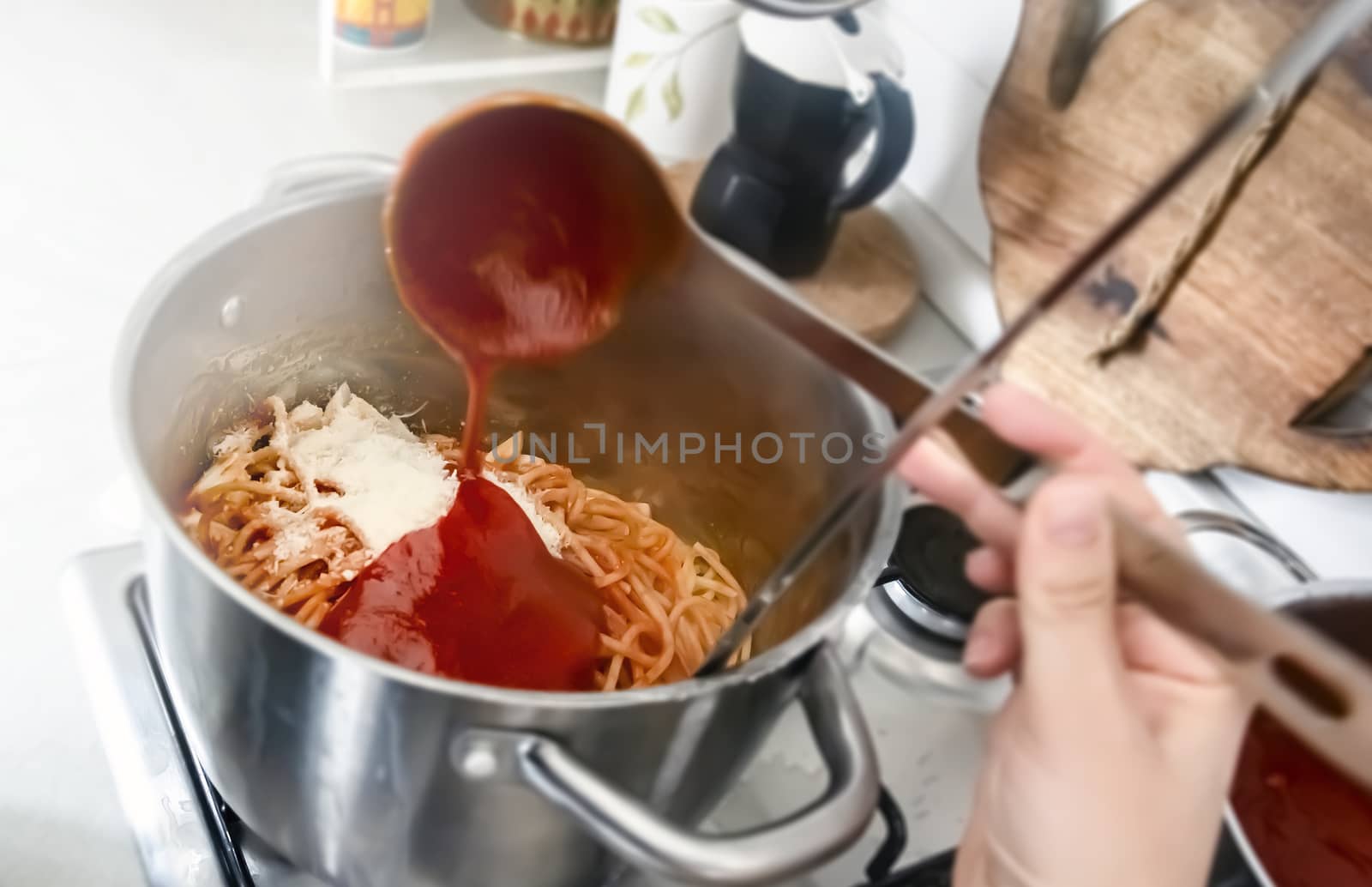Seasoning a pan full of freshly cooked spaghetti by pouring the tomato sauce with a steel ladle. Italian home cooking.