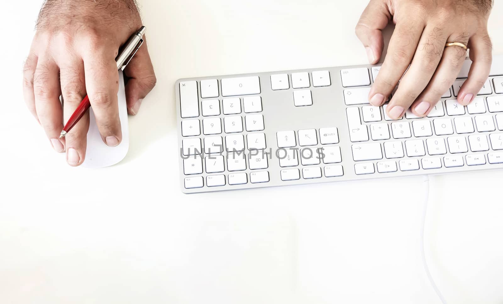 a male while using the computer keyboard and mouse holding out a red pen in his right hand by rarrarorro