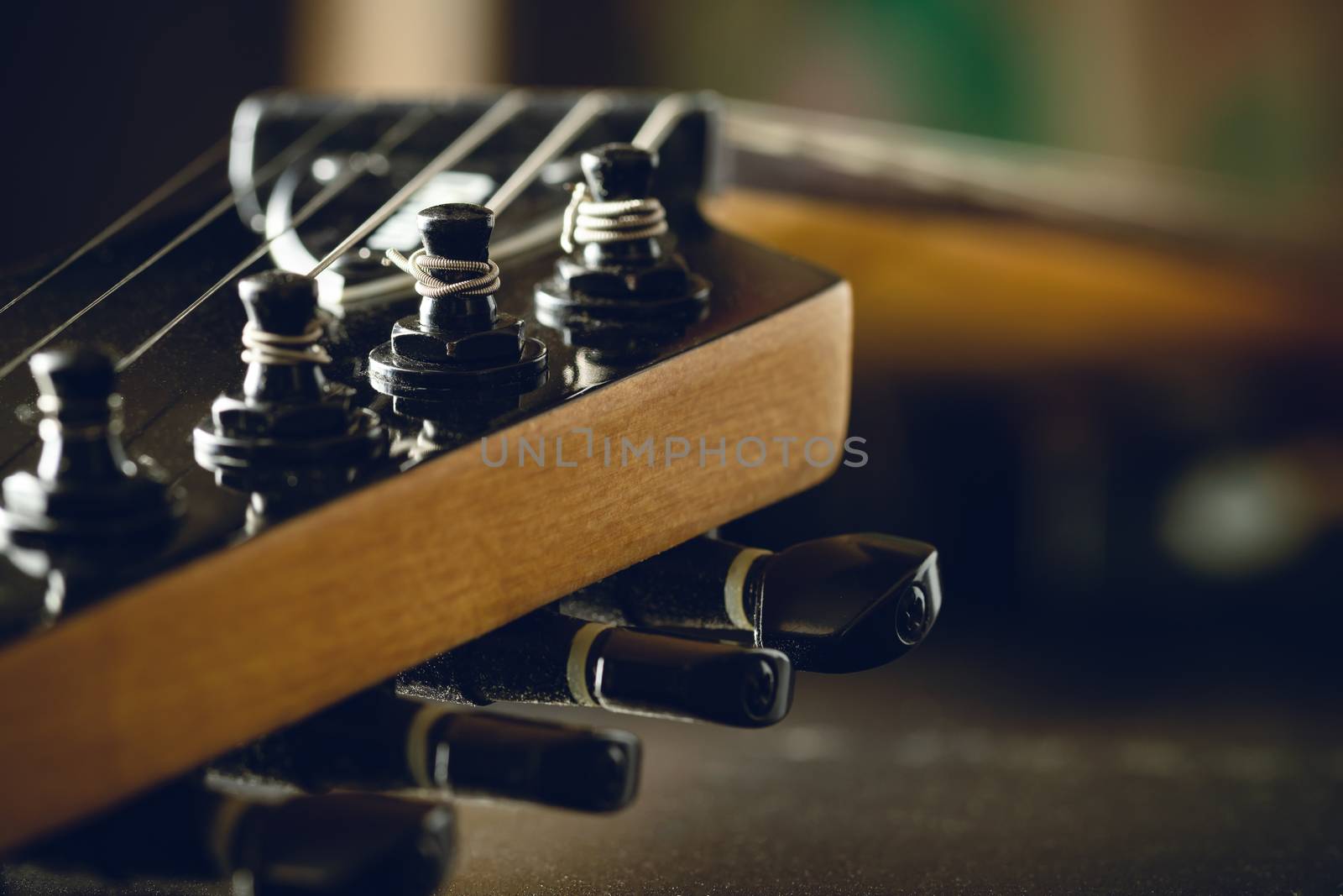 Closeup tuning key on the headstock of the black electric guitar in dark background and morning light. Copy space on the right. Concept of good memory About retro musical instruments and rock music.