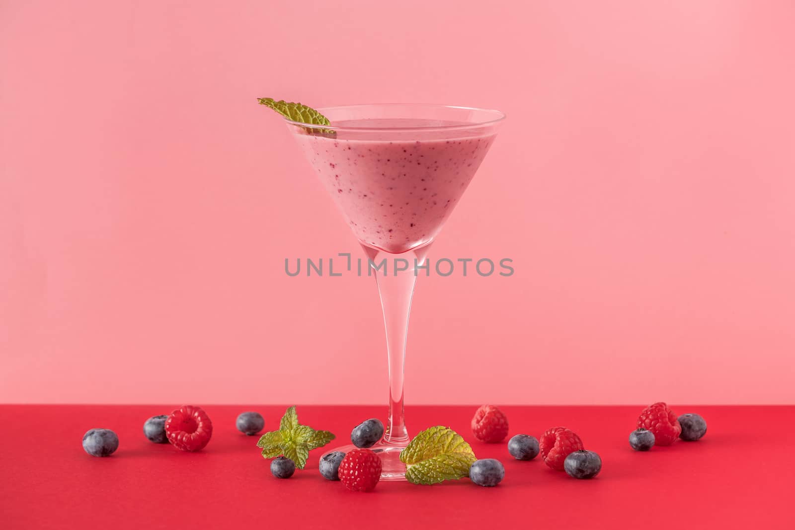 Berry smoothie cup with several blueberries and raspberries on a red and pink background. Minimalist image.