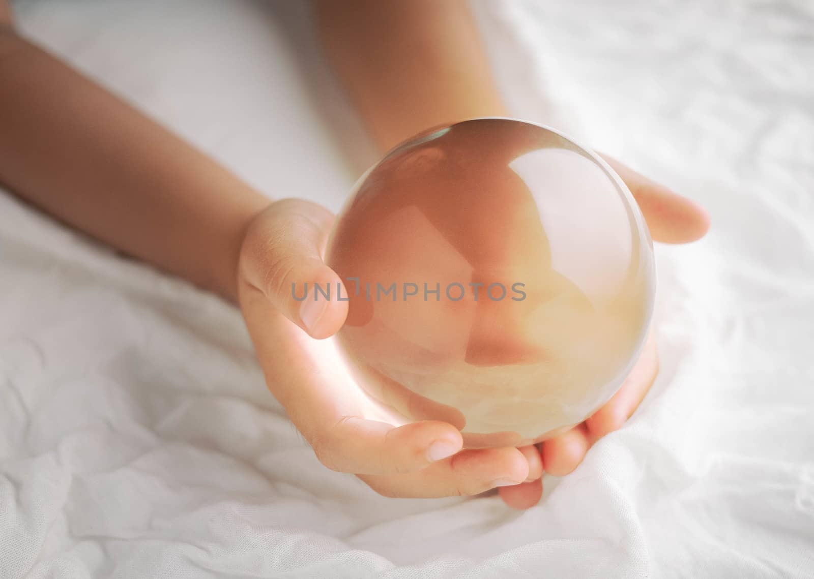 Hand holding a crystal glass ball transparent on white fabric background.