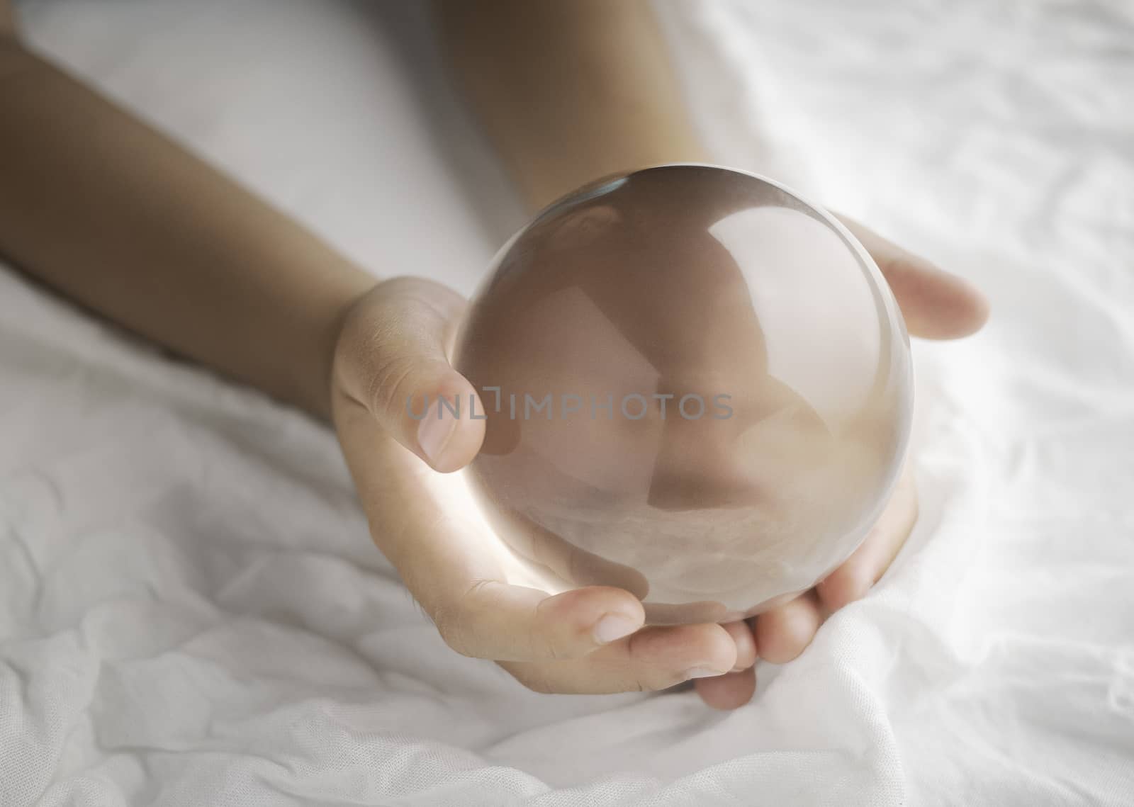 Hand holding a crystal glass ball transparent on white fabric ba by TEERASAK