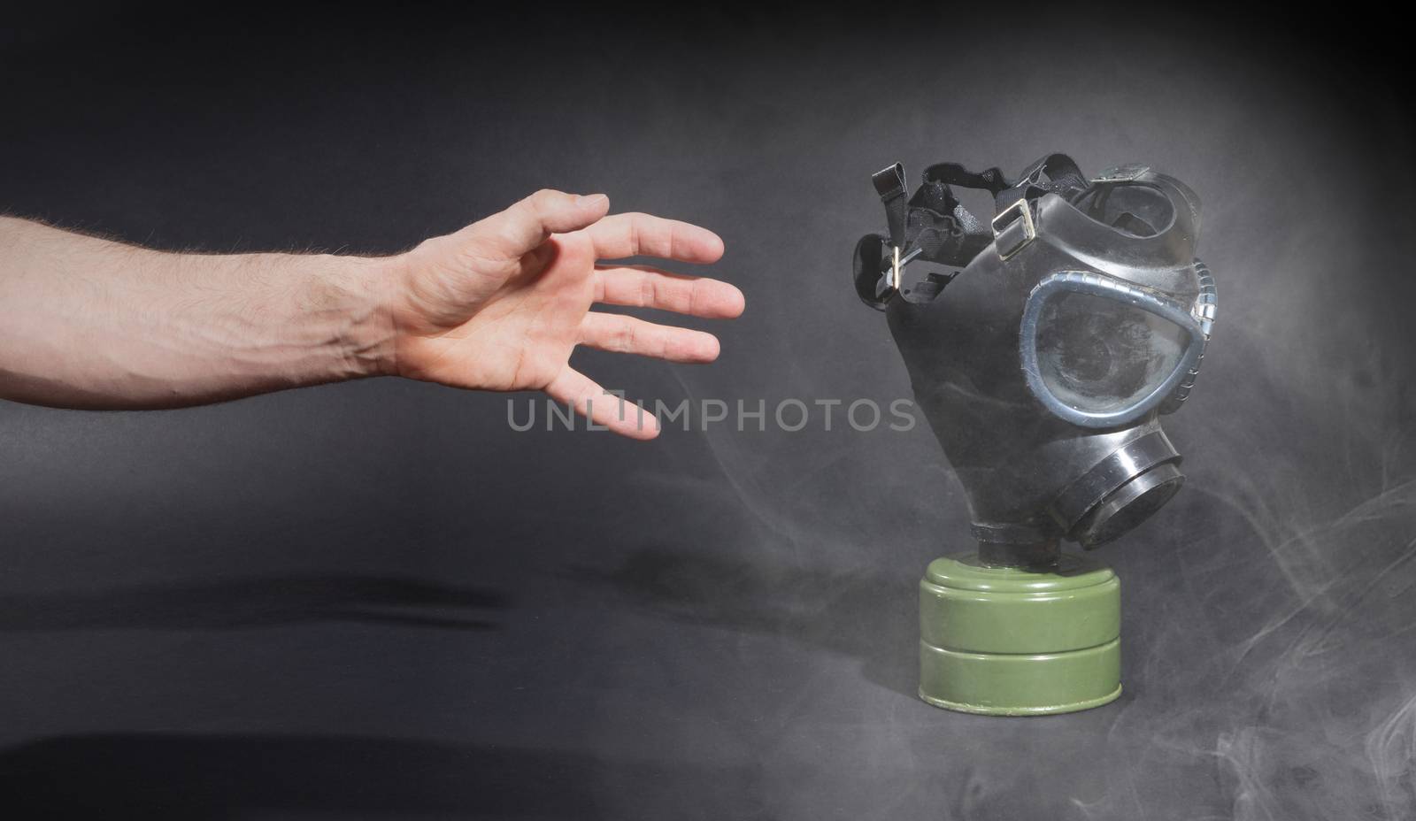 Man in room filled with smoke, trying to reach for vintage gasmask - Isolated on black - Green filter