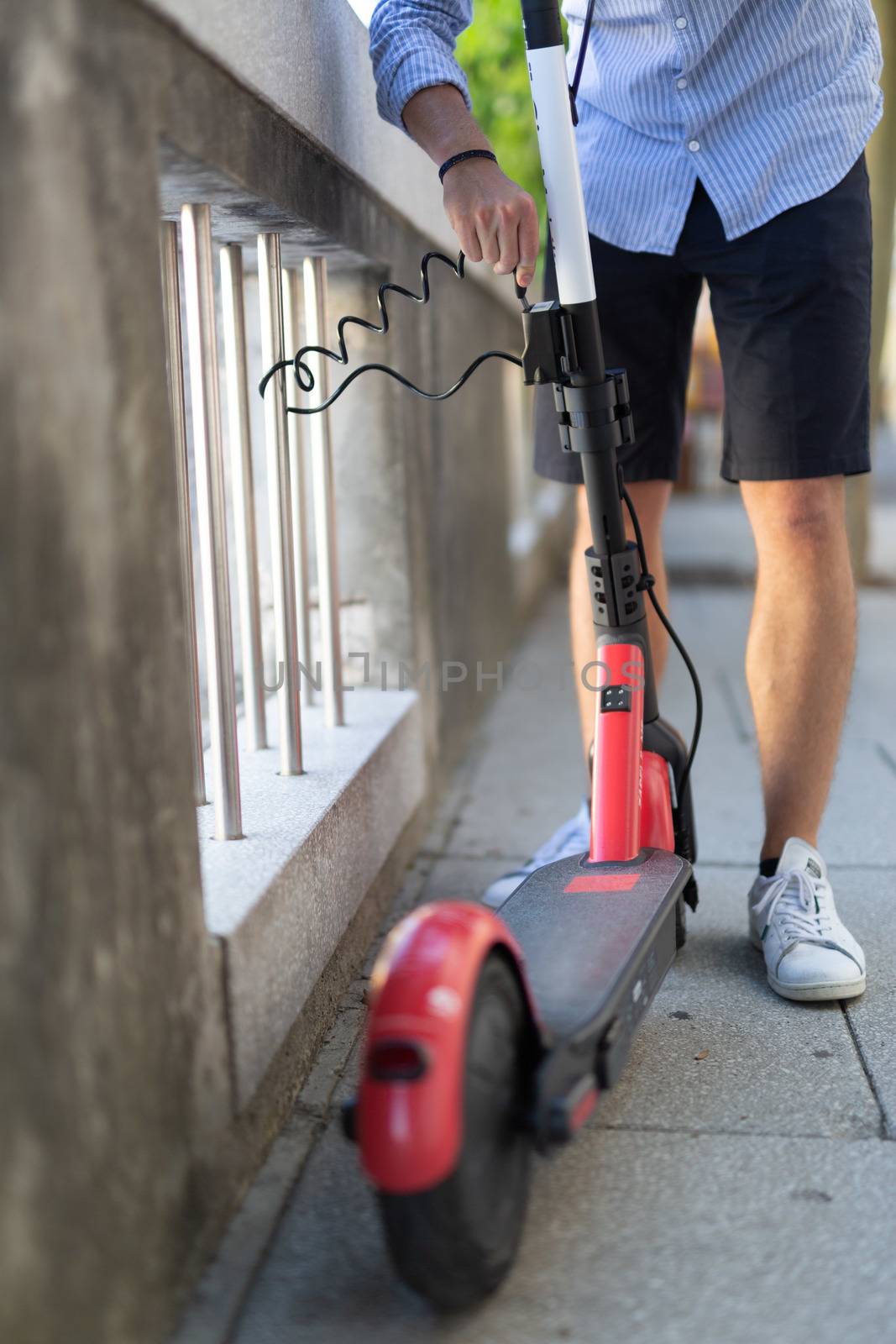 Male user safely parking electric scooter and locking it to a fence. Eco friendly green modern urban mobility concept of sharing transportation with electric scooters for rent in Ljubljana, Slovenia.