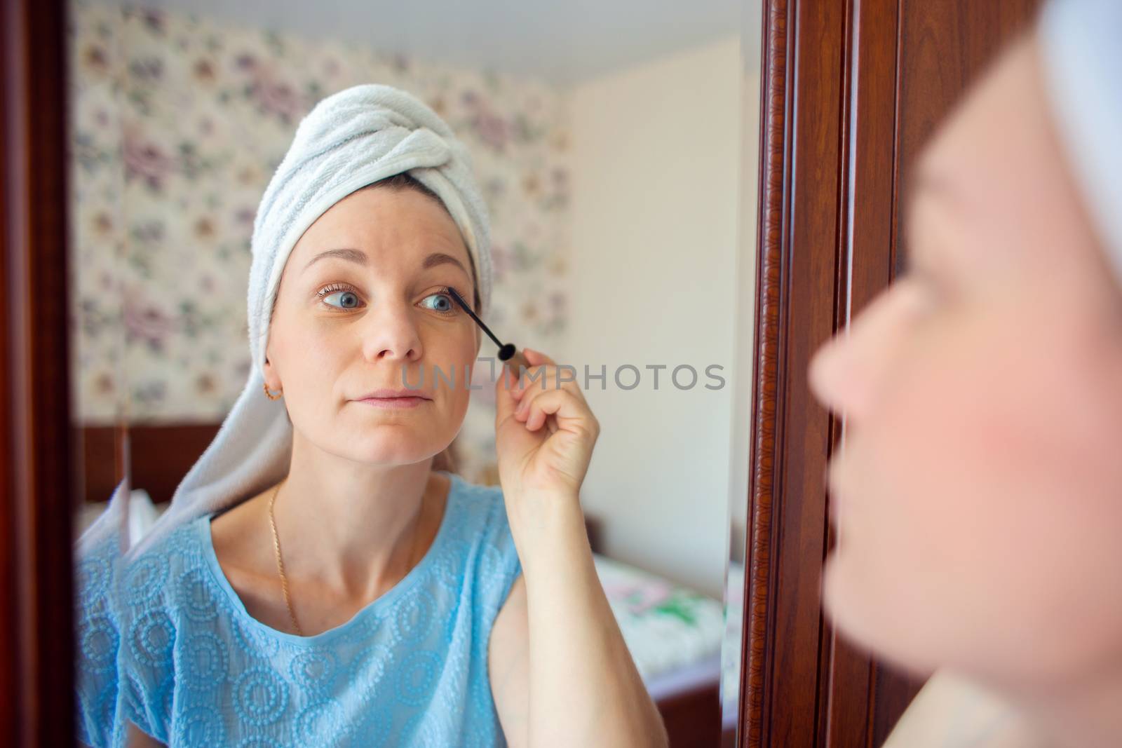 A girl with a towel on her head paints her eyelashes with mascara. The woman is going to work. Morning toilet.
