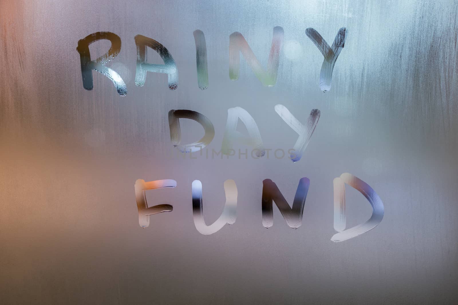 words RAINY DAY FUND written by hand on wet glass at morning with blurry street light background.