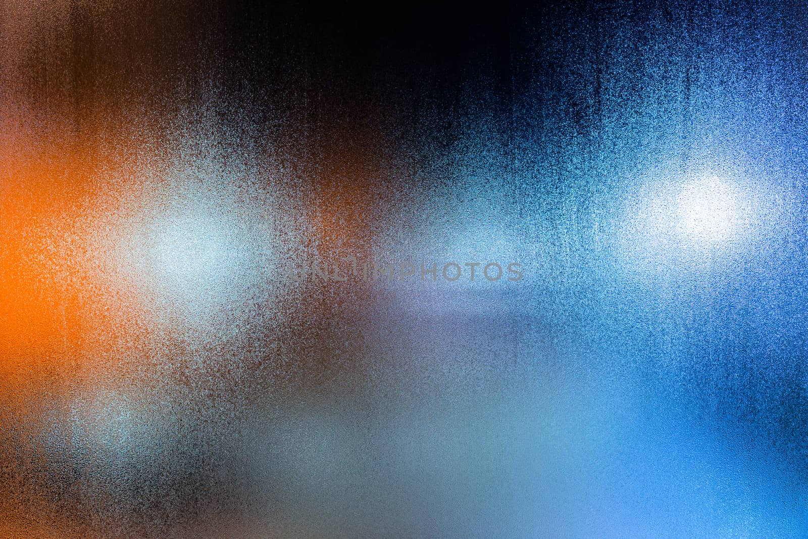 an abstract background of night street lights through wet glass with water drops, close-up with selective focus.