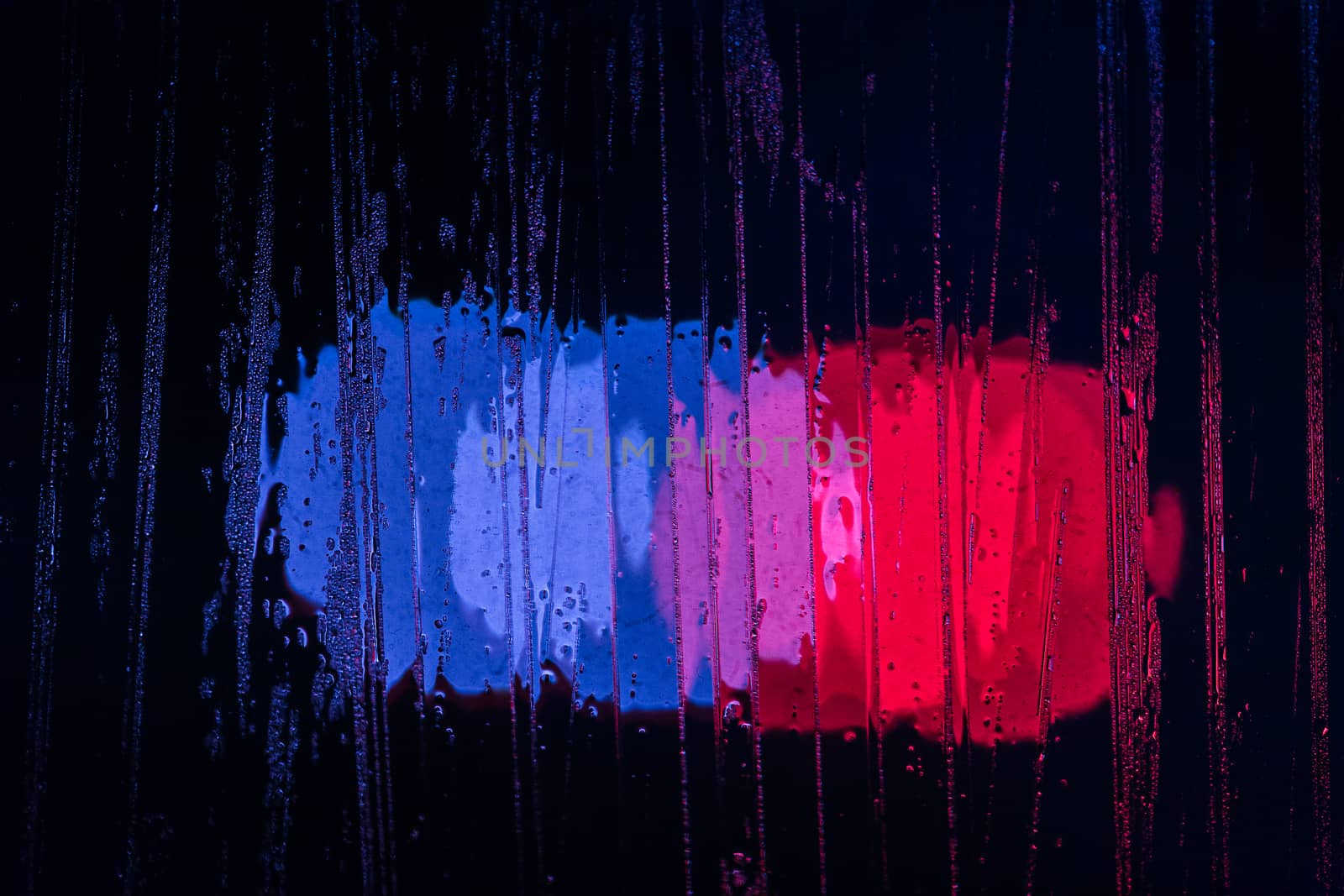 police lights bokeh trough wet glass at night close-up with selective focus abstract background