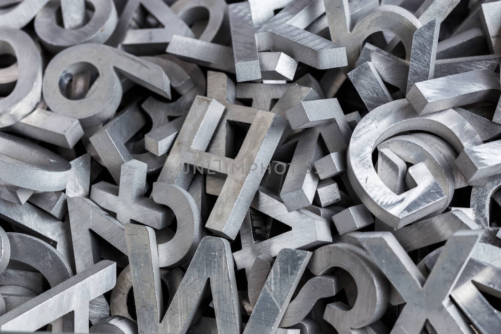 pile of silver metal alphabet characters cutted by waterjet machine - close-up view with selective focus