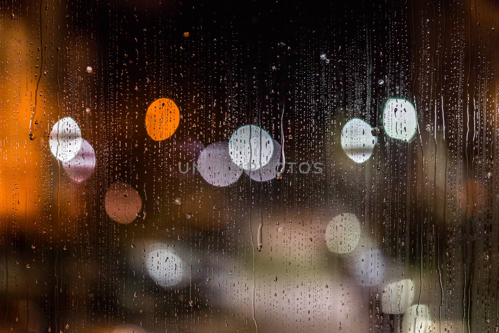 an abstract background night street lights bokeh through wet glass with water smudges, close-up with selective focus.