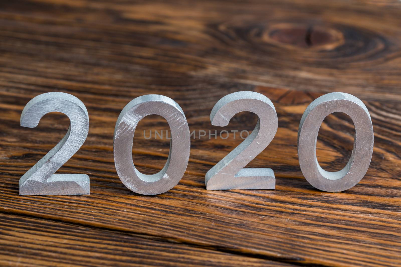 a number 2020 with white metal digits on dark brown wood background with selective focus.