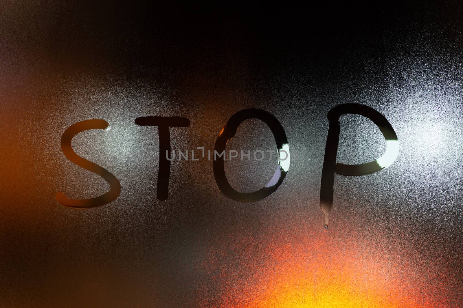 the word stop written on night wet window glass close-up with blurred background.