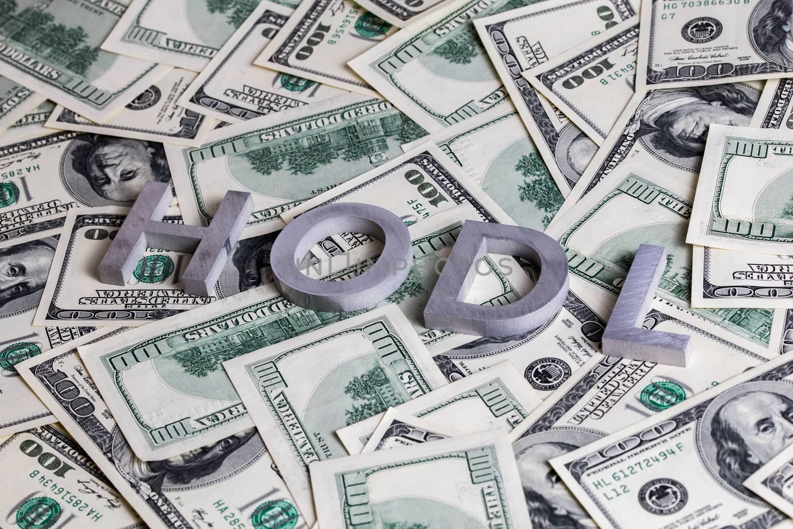 The words HODL laid with aluminium letters on the US dollar banknotes background - with selective focus.
