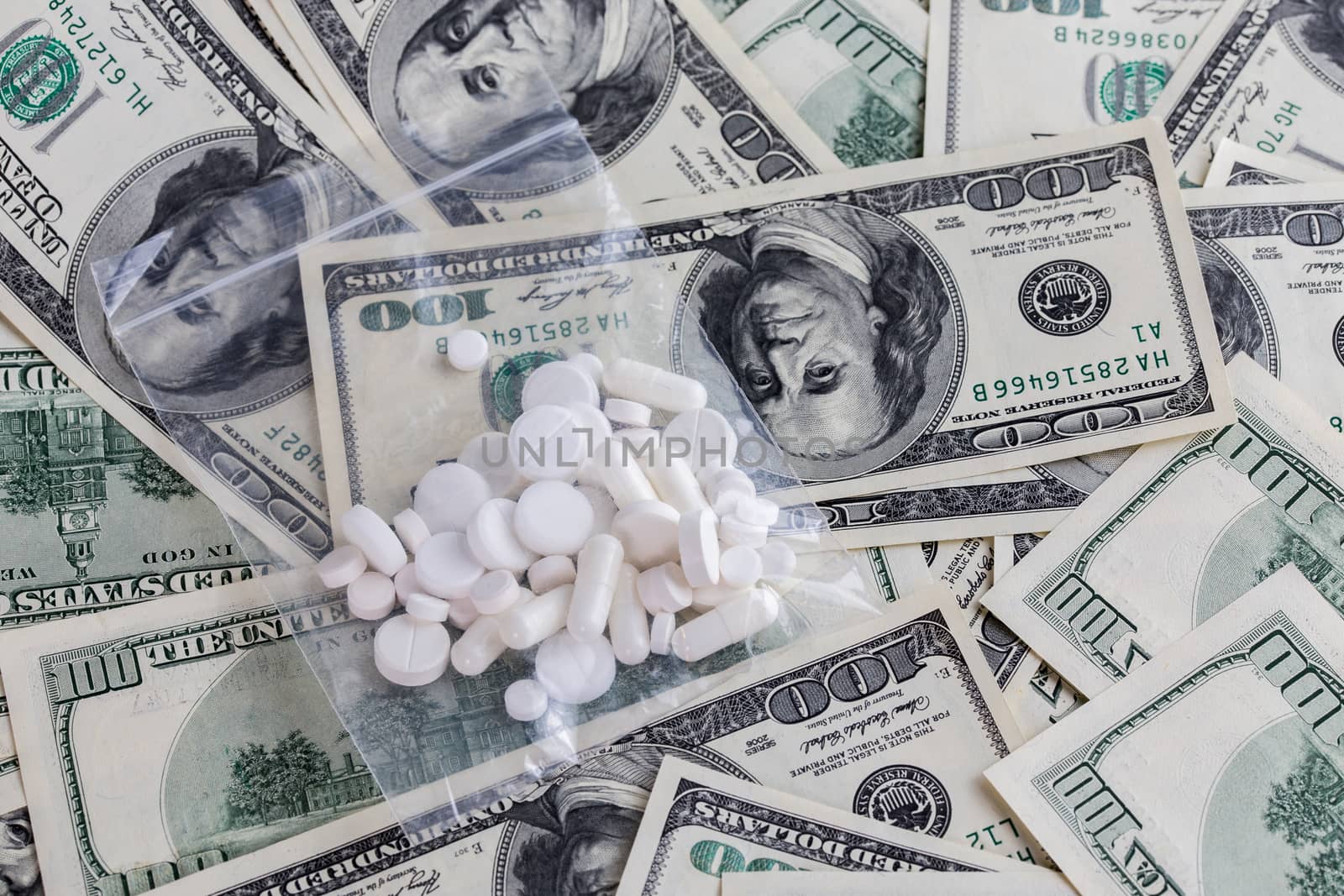 handful of white pills in small transparent plastic bag on dollar bills close-up with selective focus