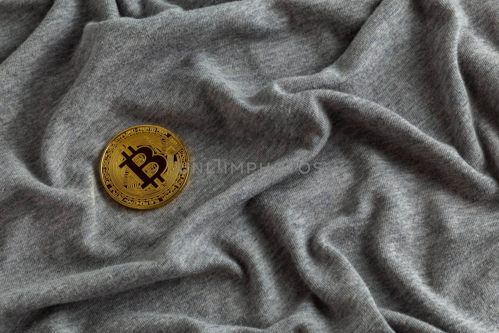 Golden bitcoin shiner on gray crumpled cotton cloth.