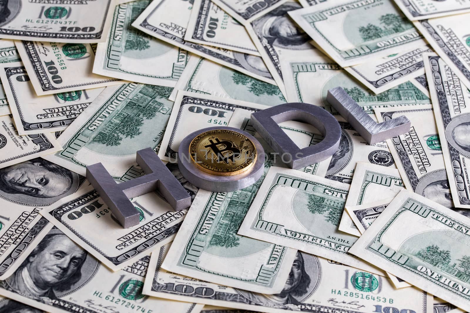 The words HODL laid with aluminium letters and bitcoin shiner on the US dollar banknotes background - with selective focus and diagonal composition.