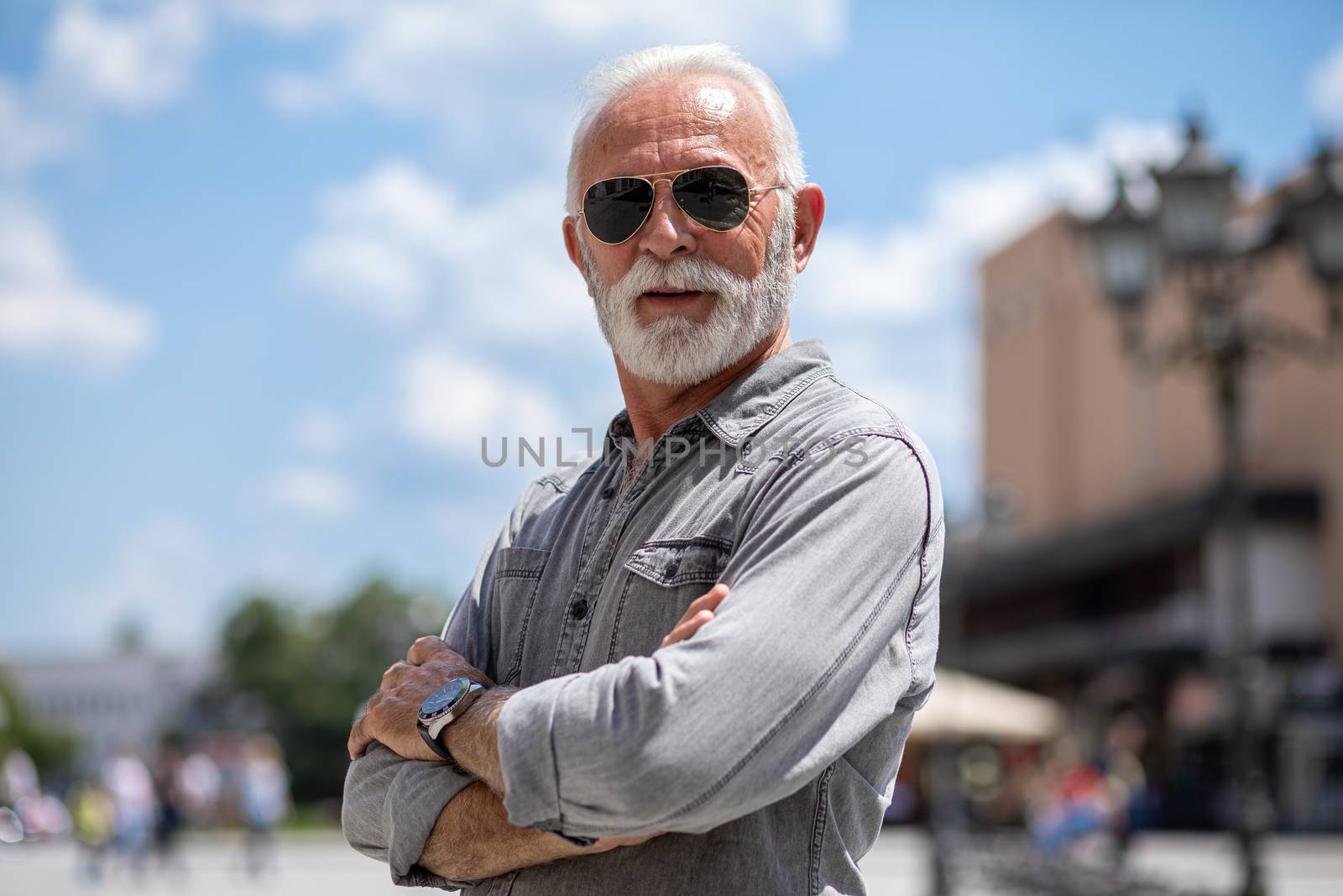 Experienced senior old man with beard and sunglass on street posing and smiling, portrait
