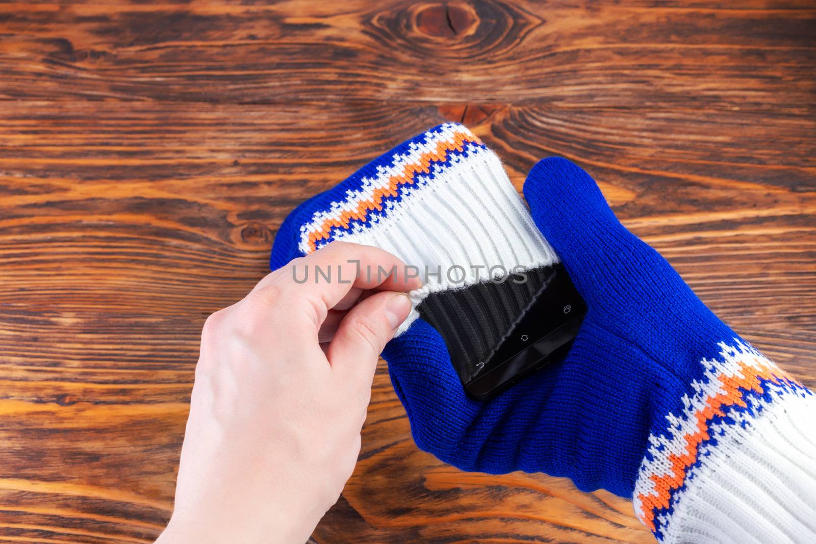 hand putting a cellphone into white-blue mittens with selective focus.