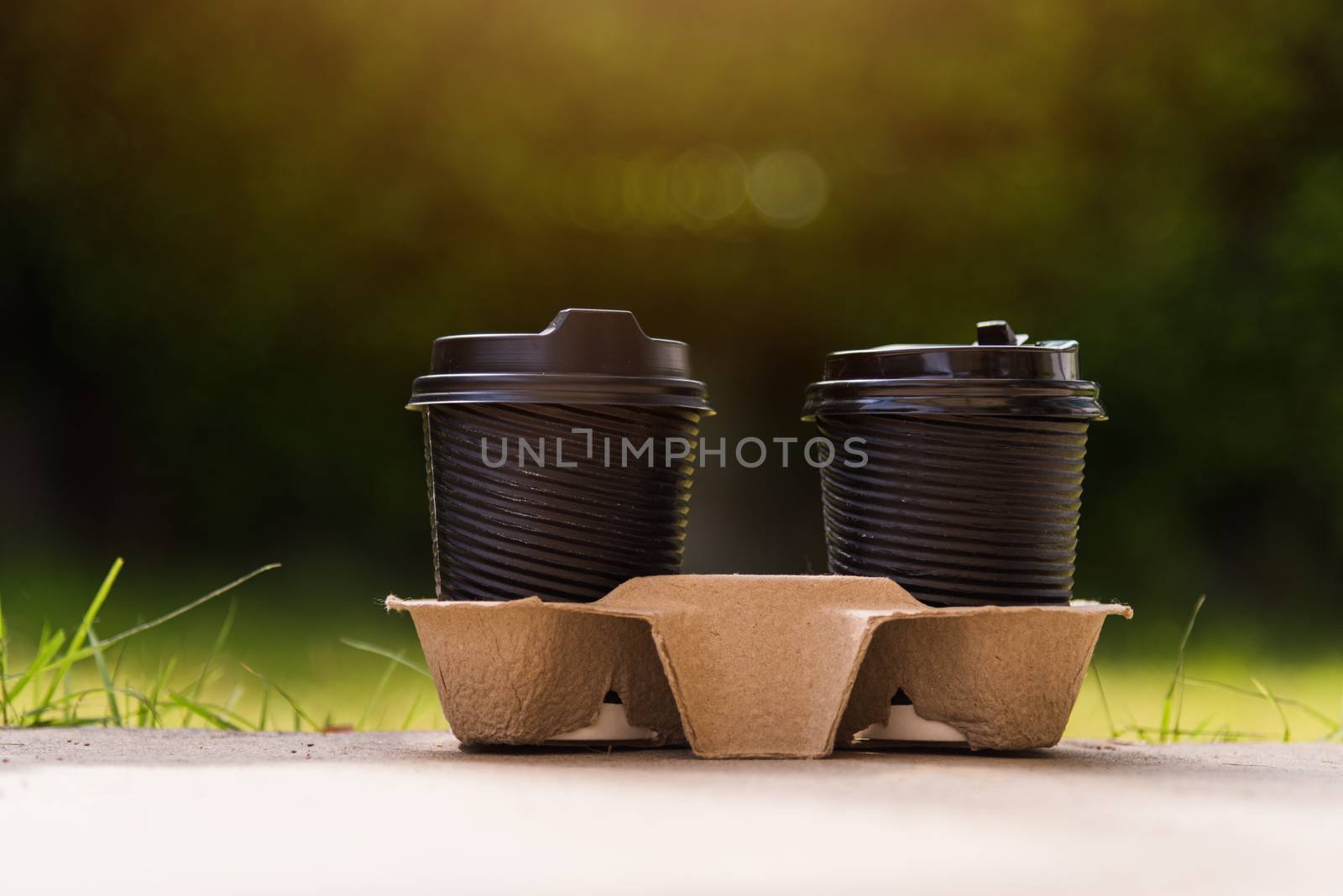 Close up of two black paper cups hot coffee to takeaway on the floor outside the cafe on the garden place of green leaves color background for copy space with sunlight in the morning day